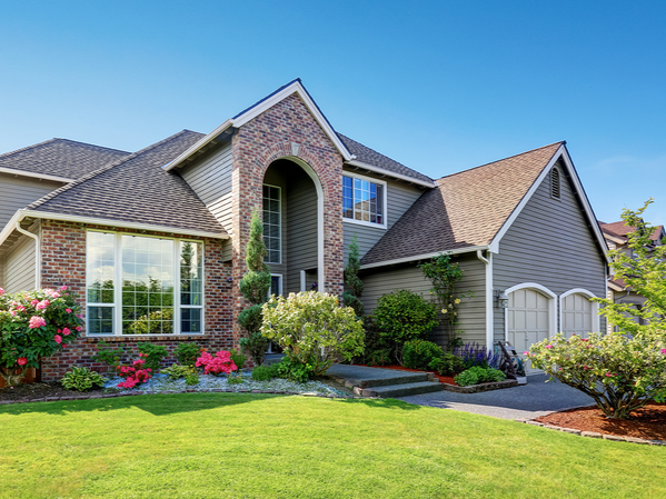 Front view of a two-story suburban house with brick and siding exterior, well-maintained lawn, and landscaped garden with bushes and flowers.
