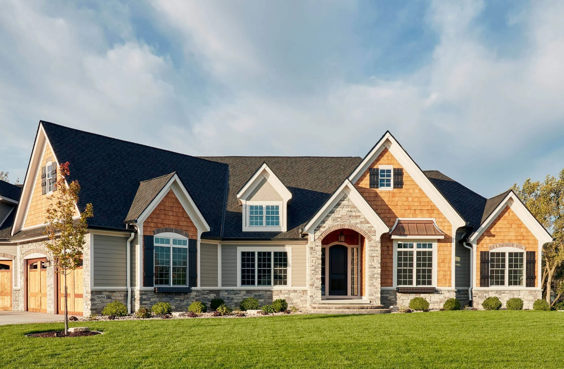 Front view of a large house with multiple gabled roofs, brick and siding exterior, and well-maintained lawn.