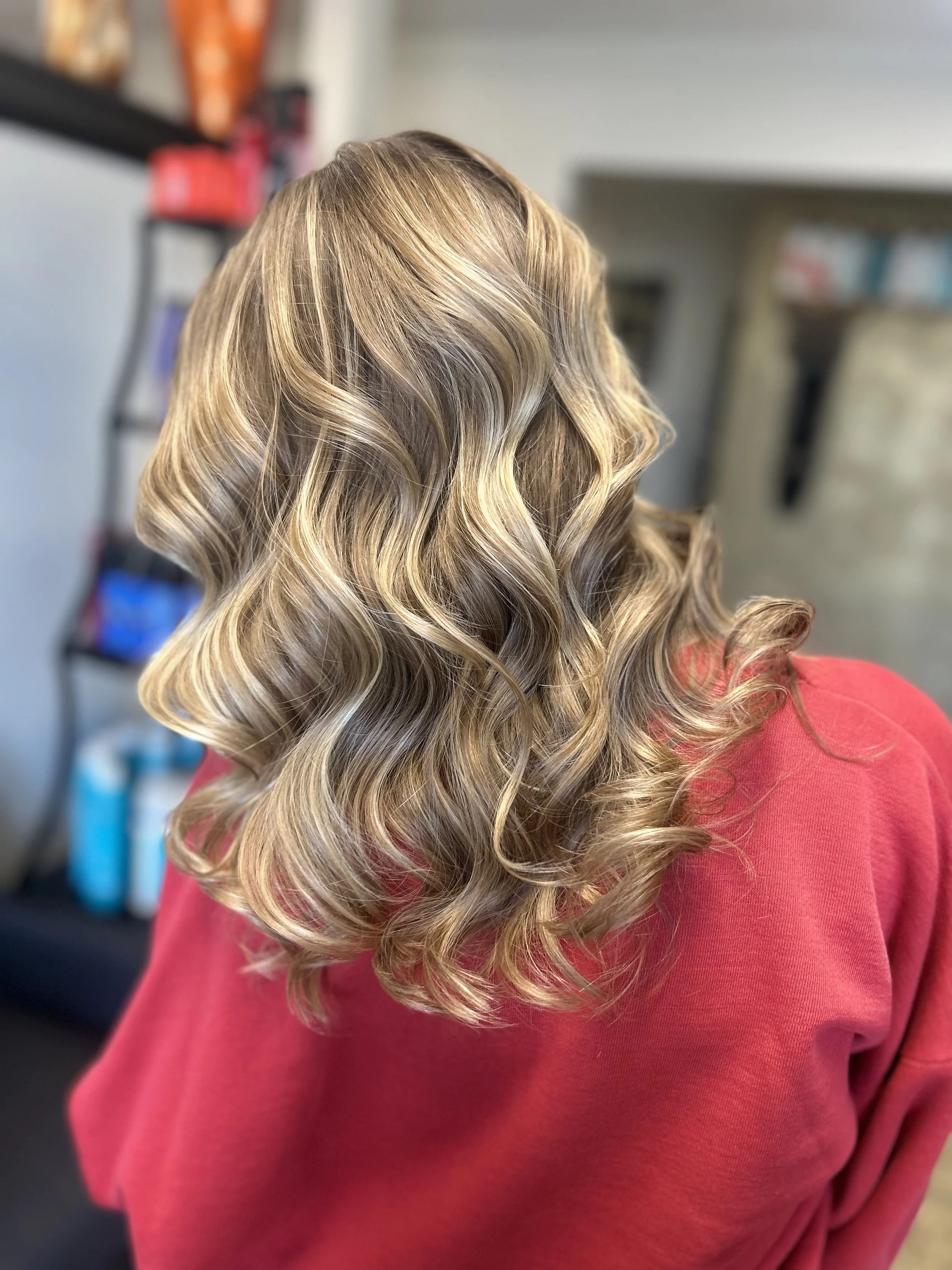 Side view of a woman with shoulder-length blonde hair styled in soft curls, wearing a red top.