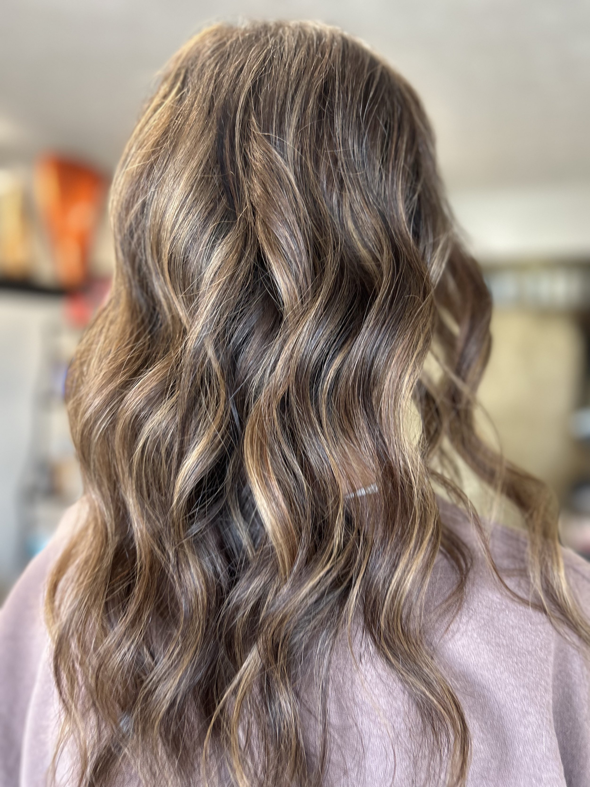 Long, wavy hair with blonde highlights and darker roots, worn by a person with a pink shirt.