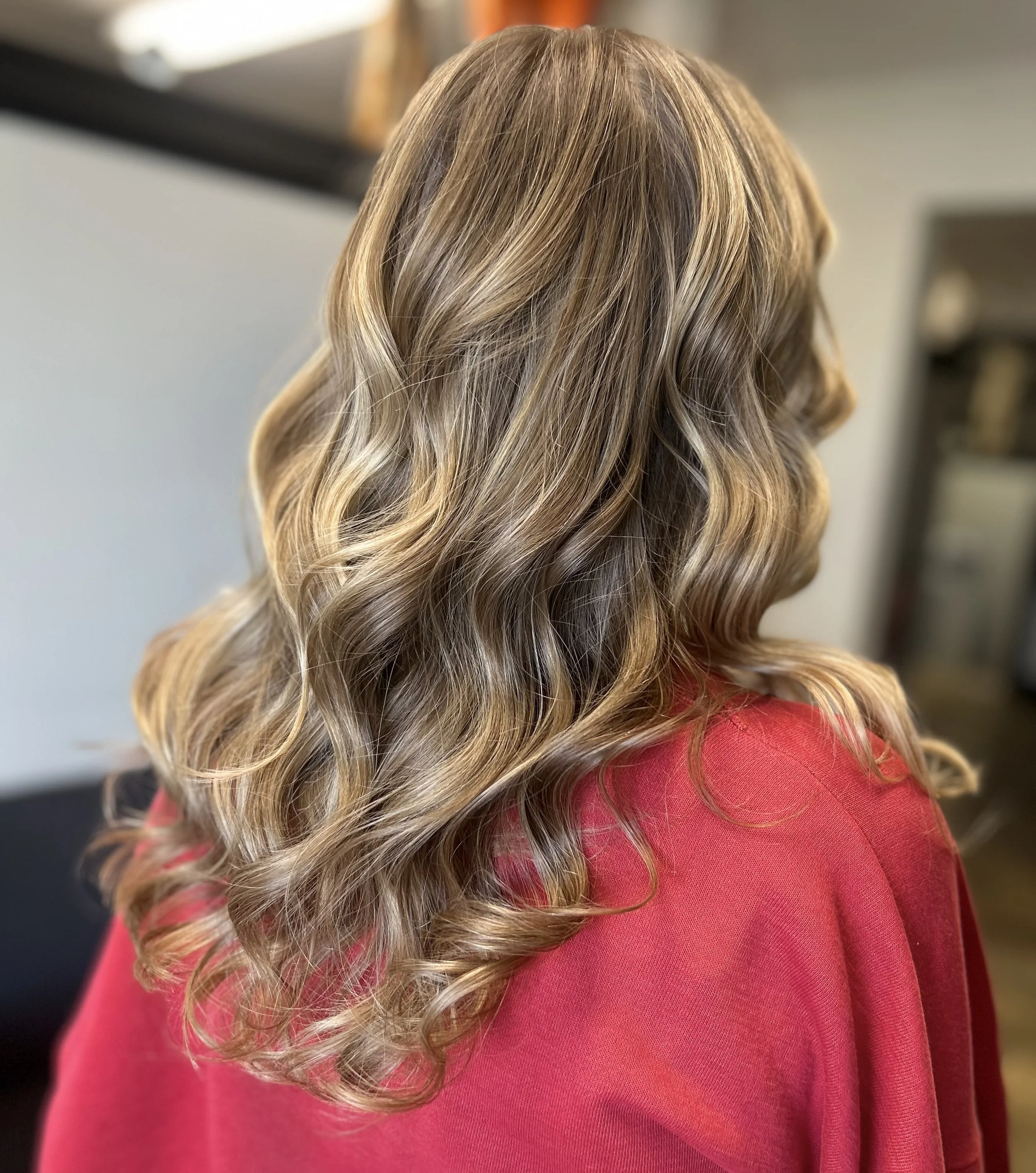 Close-up of a woman with long, blonde, wavy hair wearing a pink sweater.