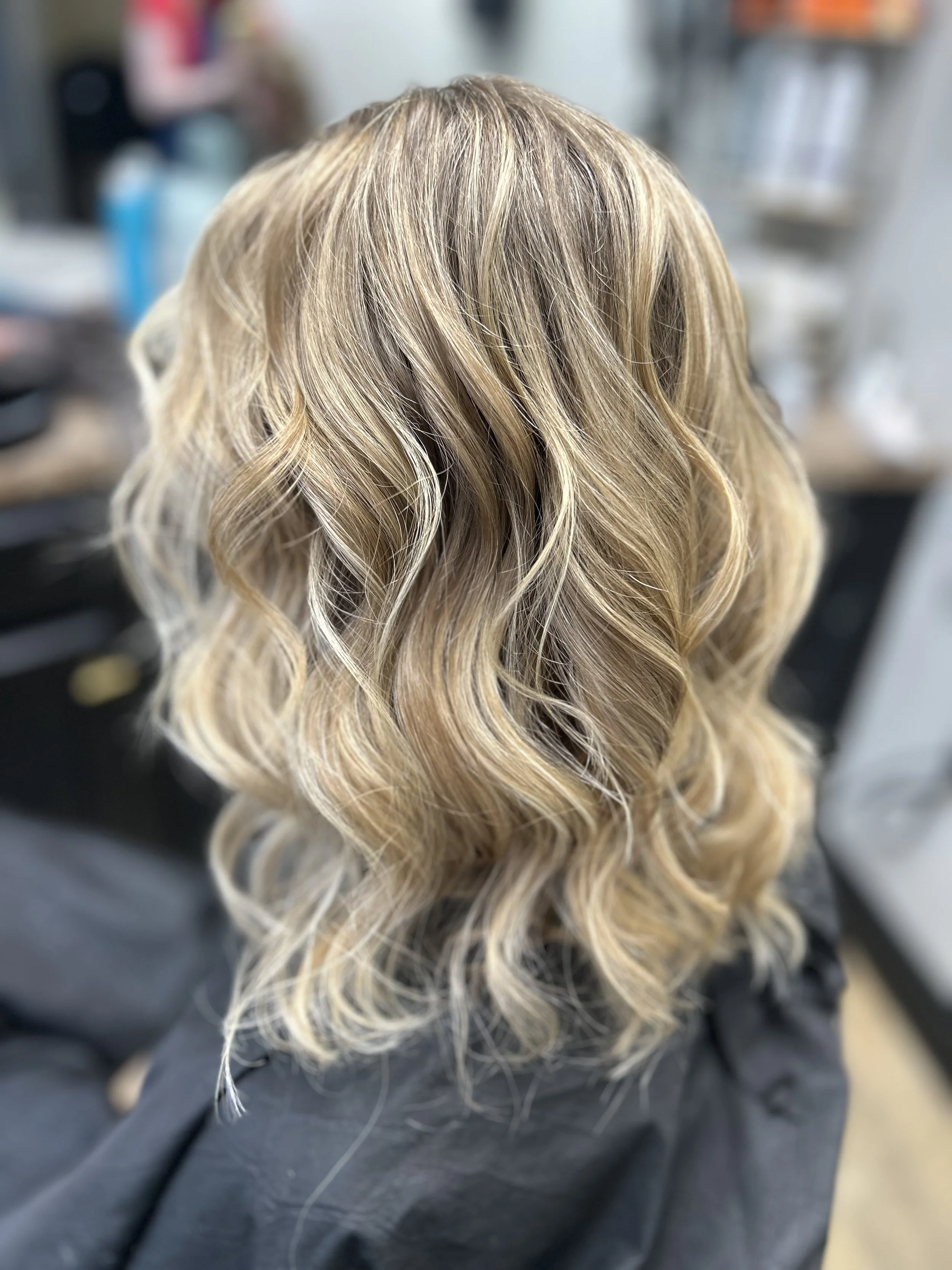 Back of blonde hair styled in loose curls, with a blurred background.