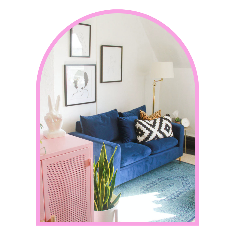 A cozy, Nashville therapy office with a blue velvet sofa, decorative pillows, a white lamp, framed artwork on the wall, a pink cabinet with a rabbit sculpture, and a green plant in a white pot.