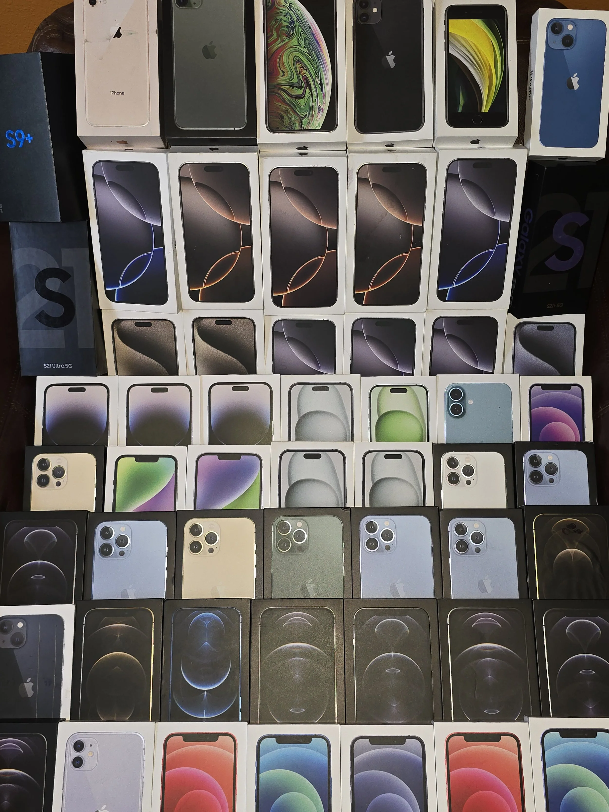 A collection of various iPhone and Samsung Galaxy smartphone boxes displayed in rows, showcasing different models and colors.