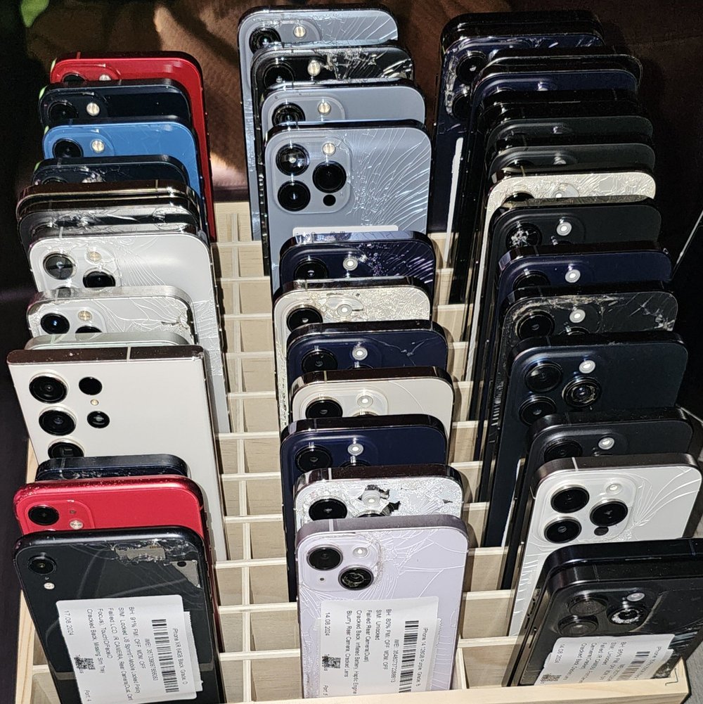 Cracked iPhones and Samsung phones displayed on a wooden stand at ShellPhone Wireless