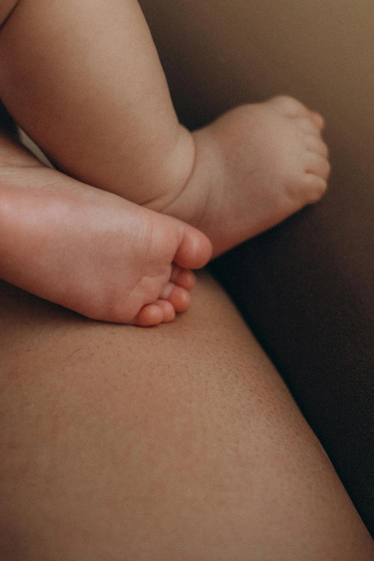 Close-up of a person's arm gently resting on their leg, with skin visible. The background is blurred, showing natural skin tones.