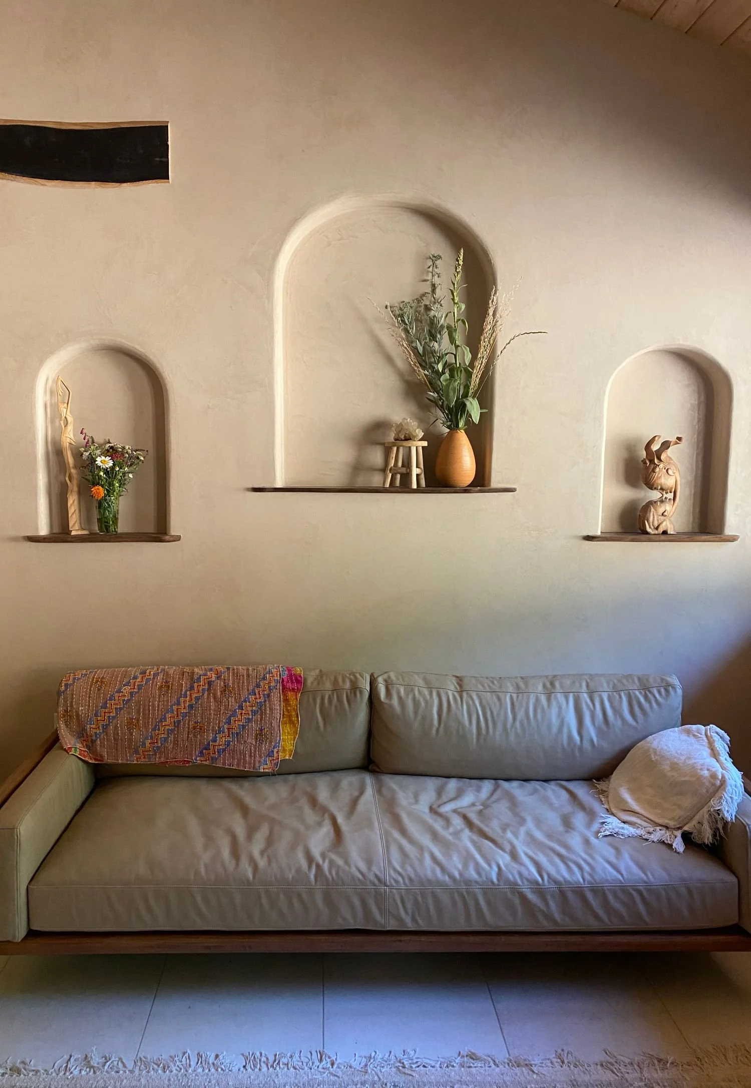 Living room with a beige sofa, decorative pillows, and a wall with built-in niches containing plants and sculptures.