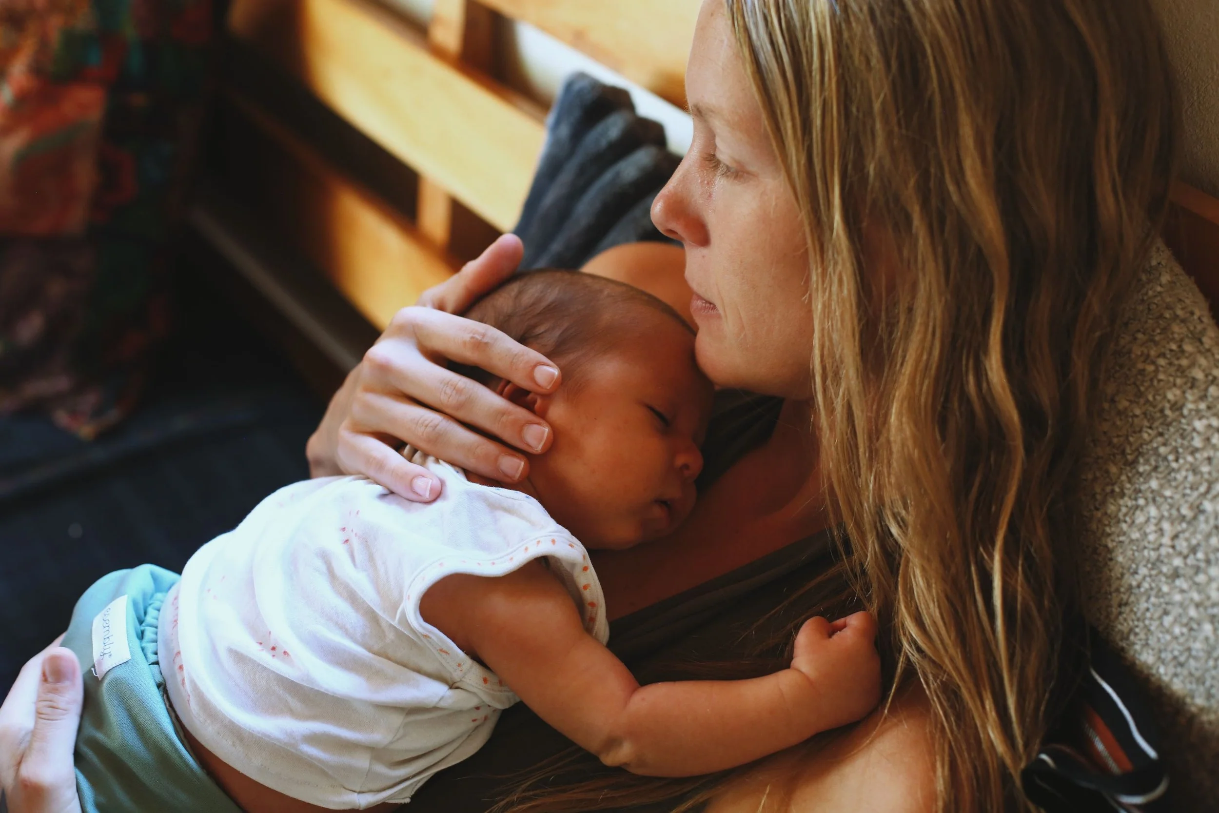 A woman with long blonde hair holding and comforting a sleeping infant.