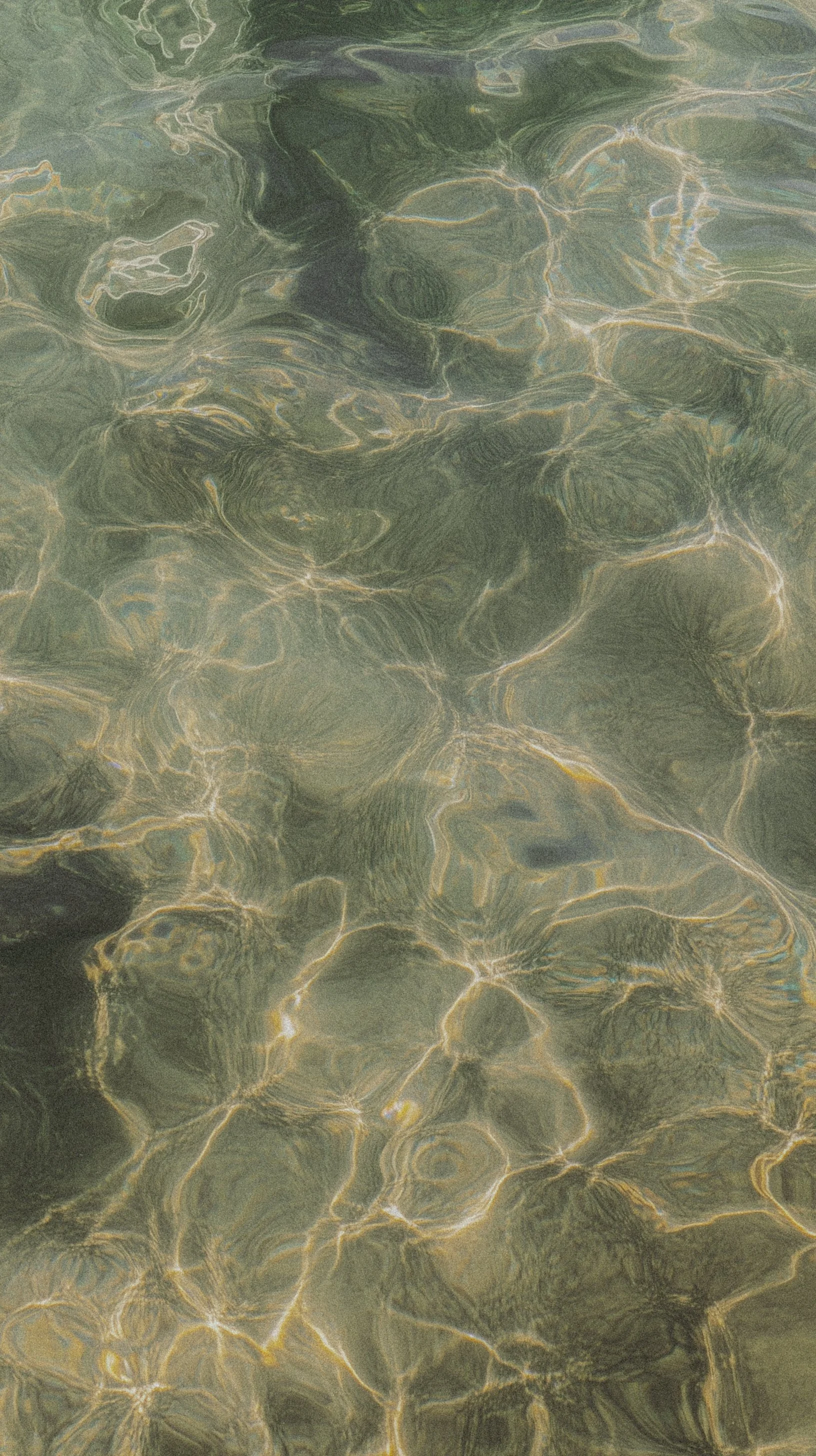 Close-up of clear water with sunlight reflecting off the surface, creating a pattern of bright, shimmering lines and ripples.