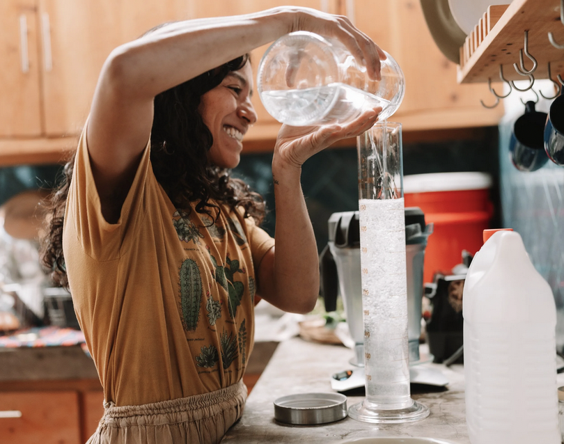 Woman pouring water from a bowl into a test tube in a kitchen.