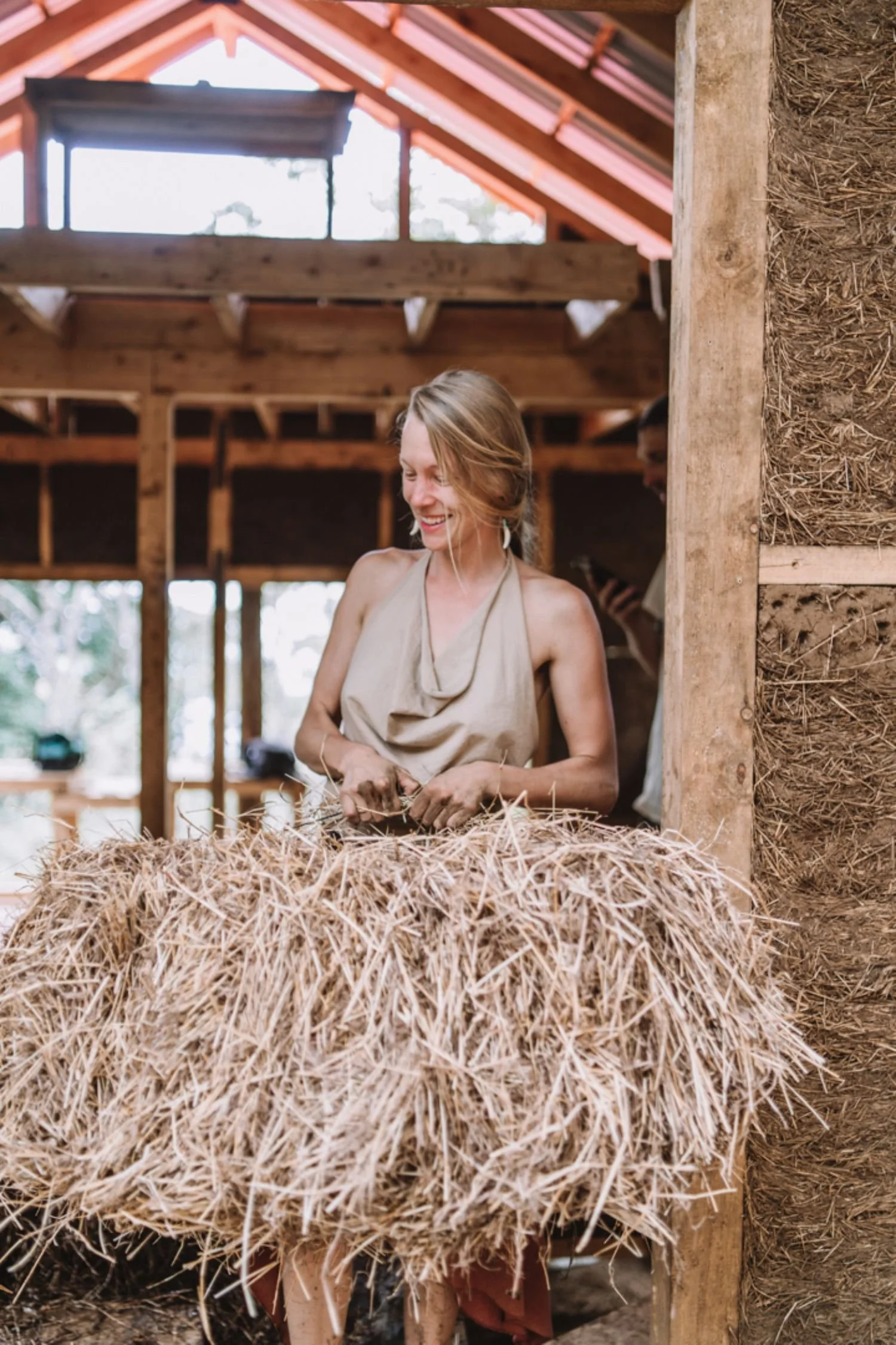 A woman smiling and working with straw inside a wooden structure under construction.