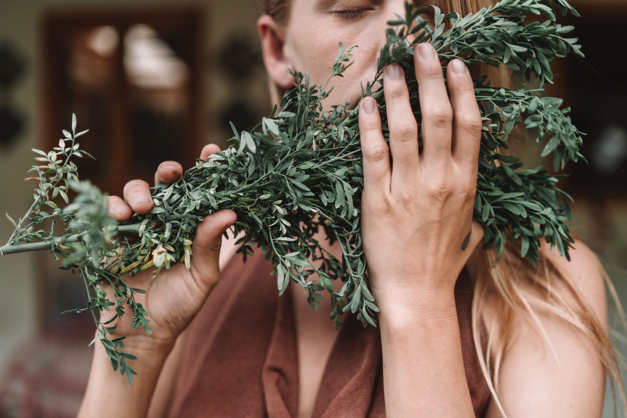 Person holding a bouquet of green leafy plants close to their face with closed eyes.