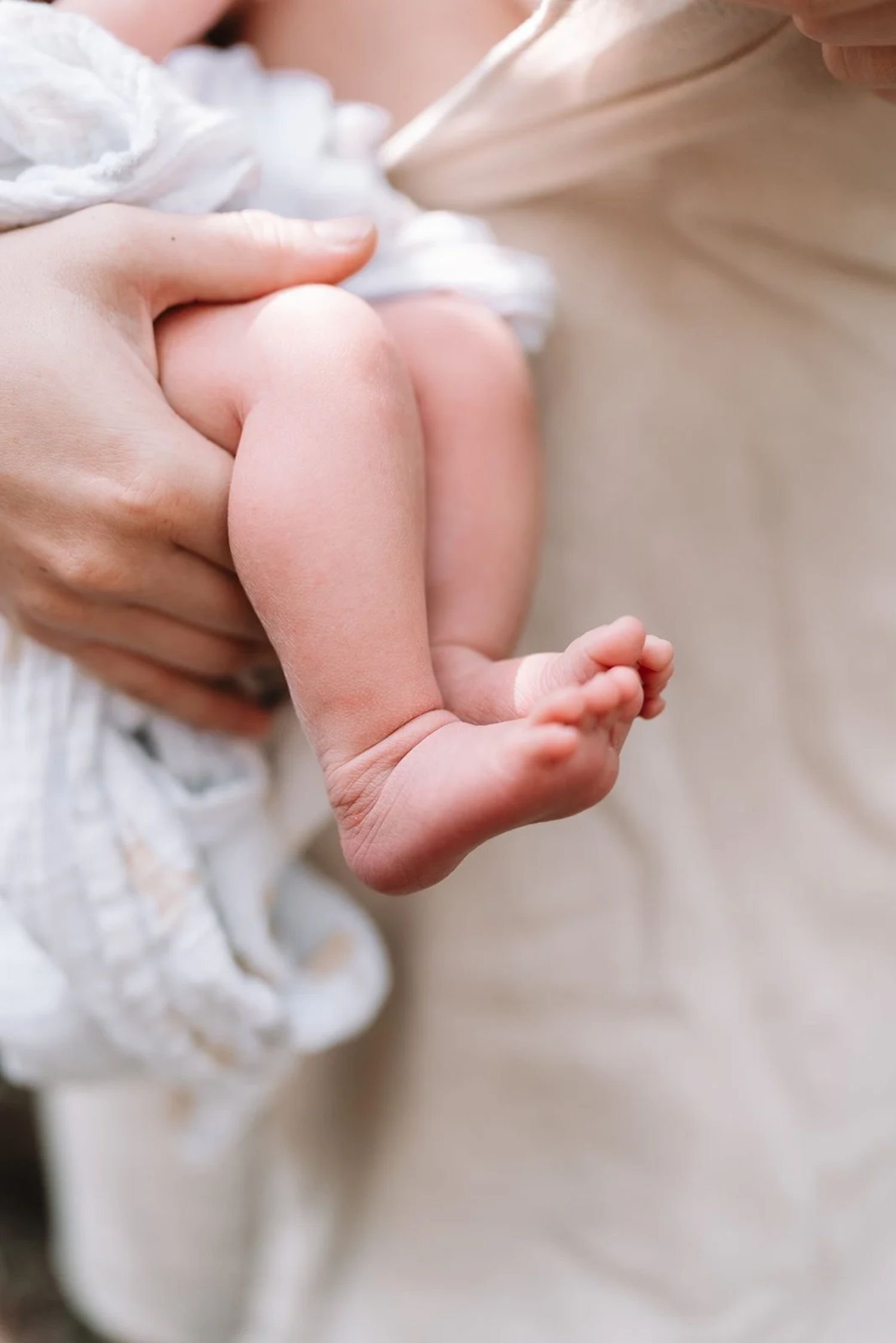 Close-up of a person holding a baby's foot with one hand, the baby is wearing a white outfit with lace details.