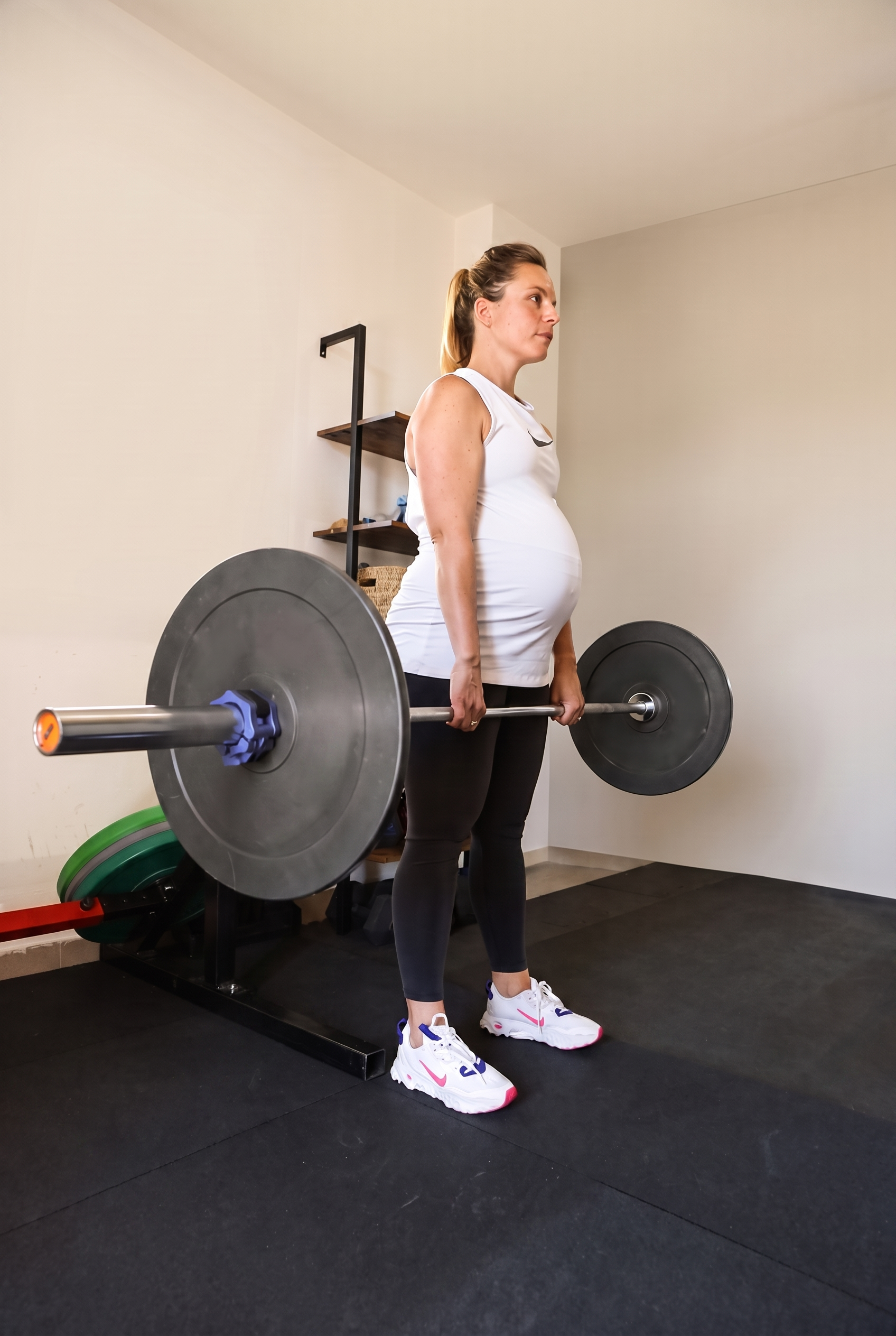 Una donna incinta si allena sollevando un bilanciere in una palestra domestica.