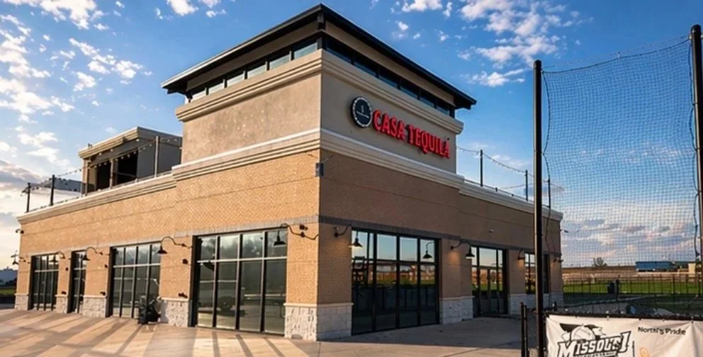 Exterior of Casa Tequila restaurant with large windows, brick walls, and a neon sign, under a blue sky with clouds.