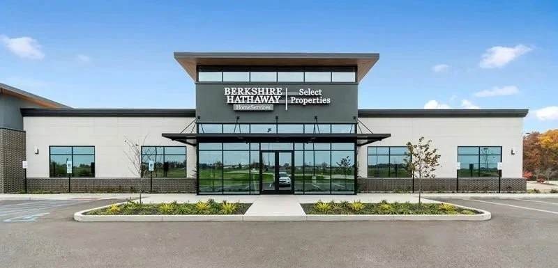 Modern commercial building with a sign reading 'Berkshire Hathaway HomeServices Select Properties' in the center of the facade, surrounded by a paved parking lot and landscaping.