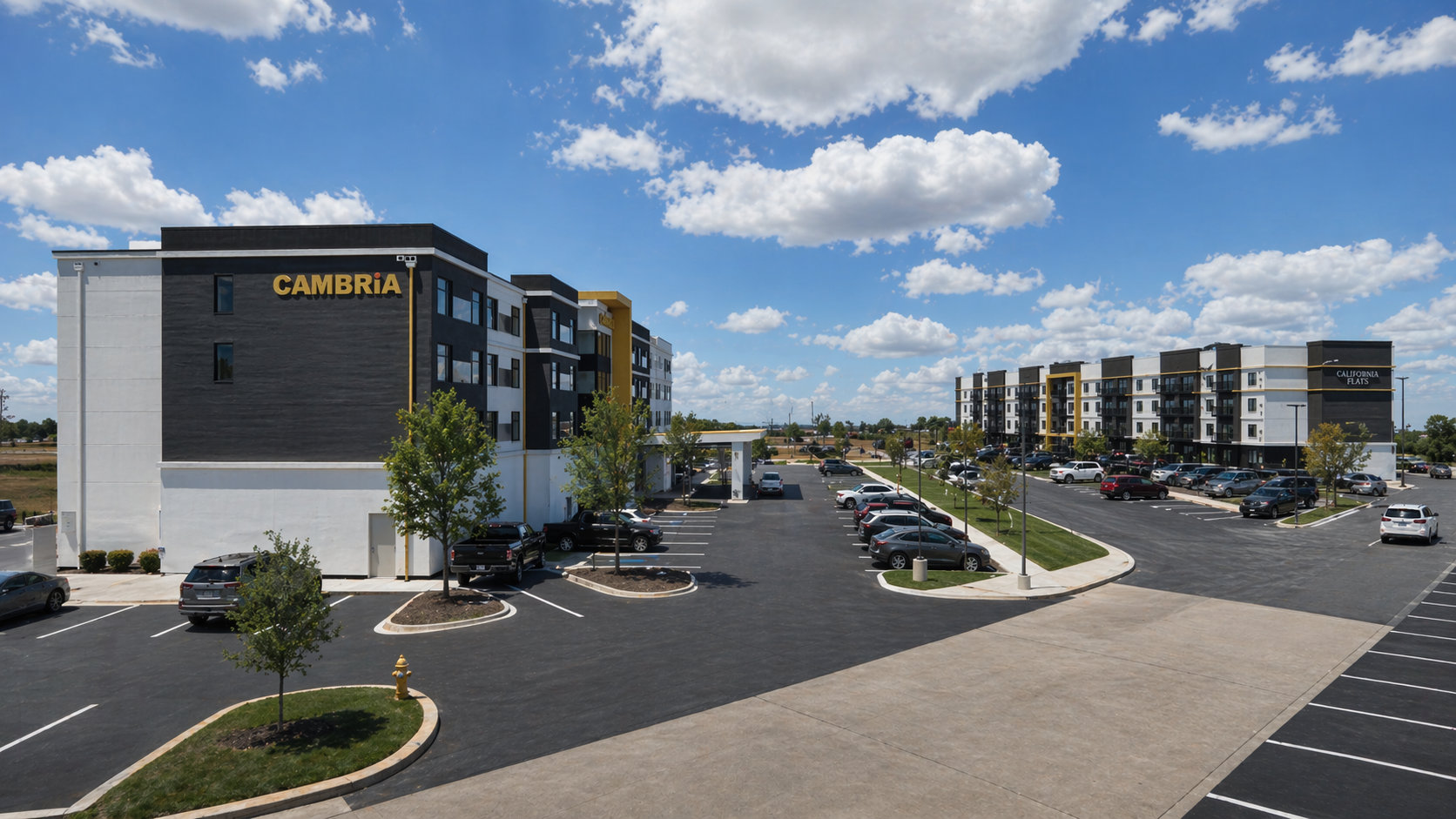 A modern apartment complex named CAMBRiA and California Flats with a large parking lot and a few parked cars under a partly cloudy sky.
