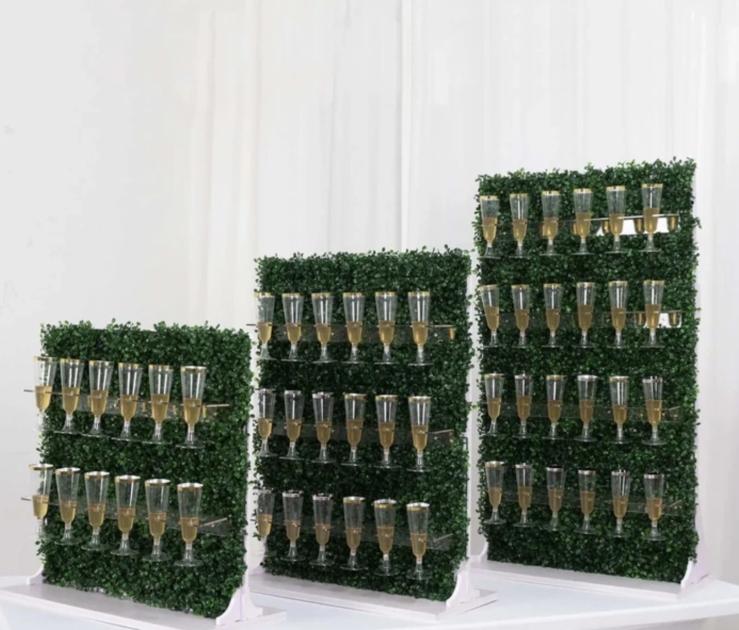Display of champagne glasses with green foliage backdrop, arranged on three white platforms.