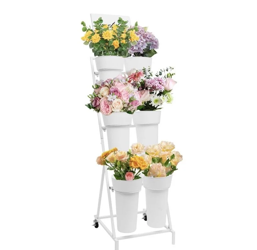 A white metal flower stand with six buckets, each holding potted and cut flowers in various colors including yellow, purple, pink, and peach.