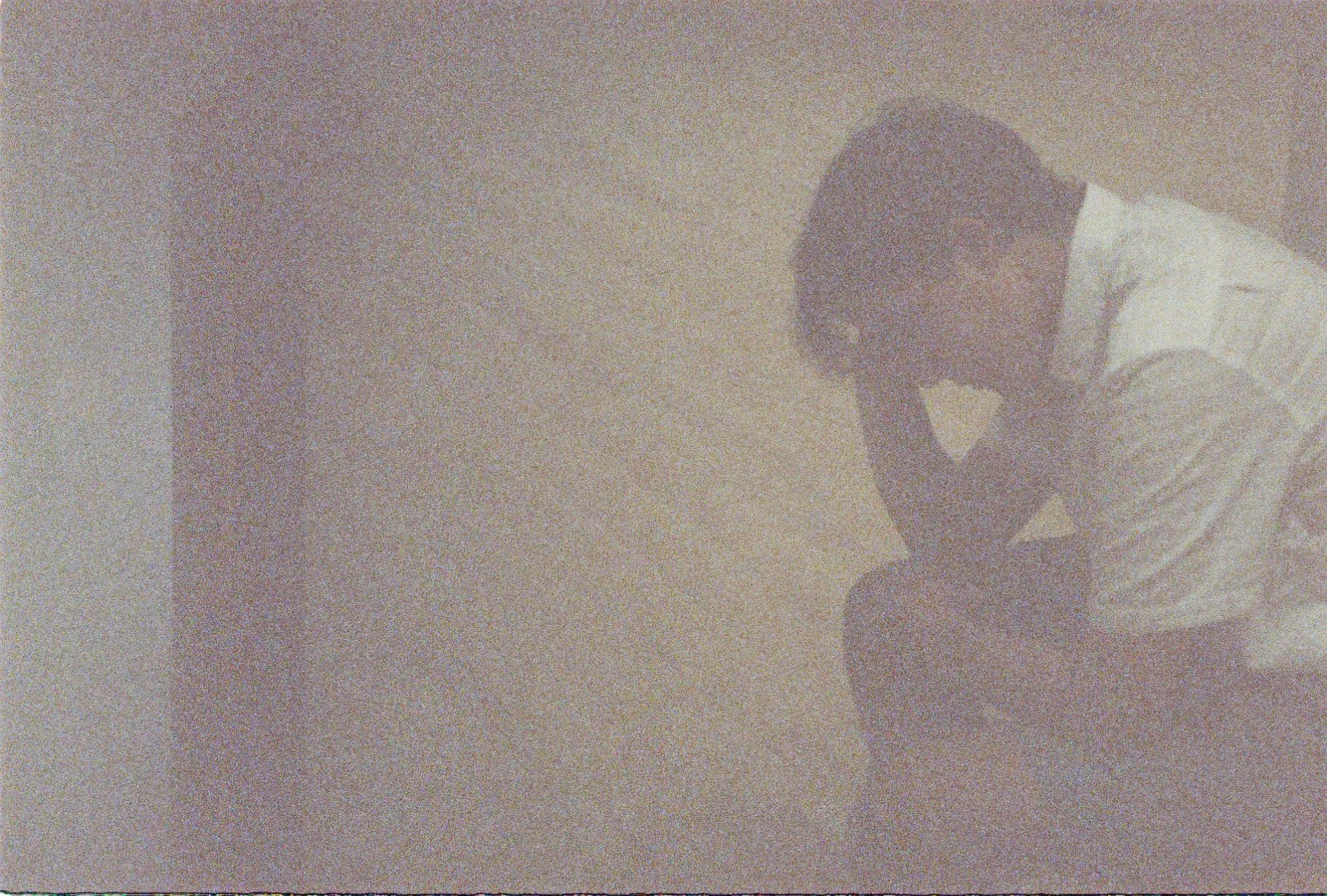 A man wearing glasses and a white shirt working or resting his head on his hand against a beige wall.