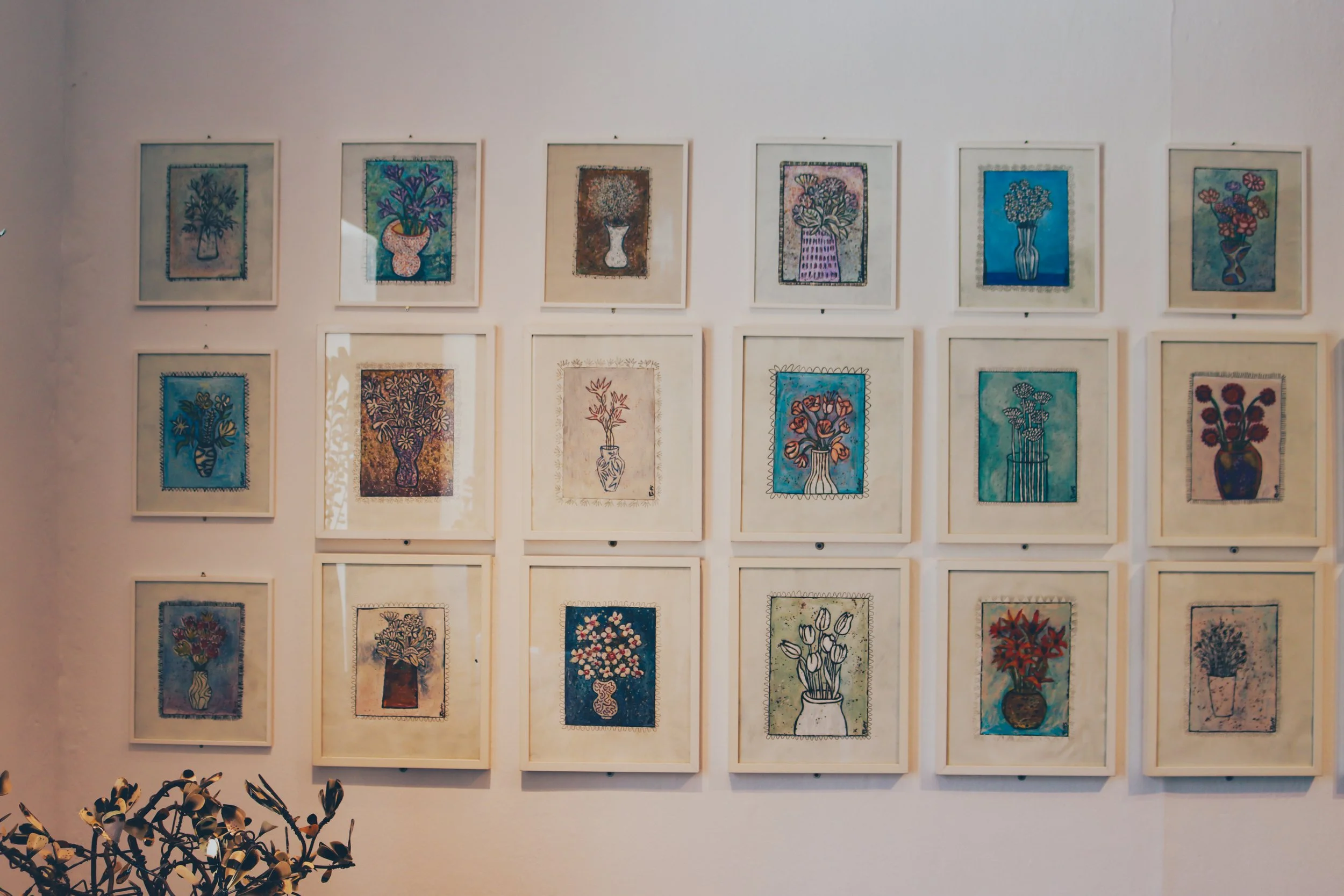 Gallery wall with multiple framed artworks of colorful flower vases.