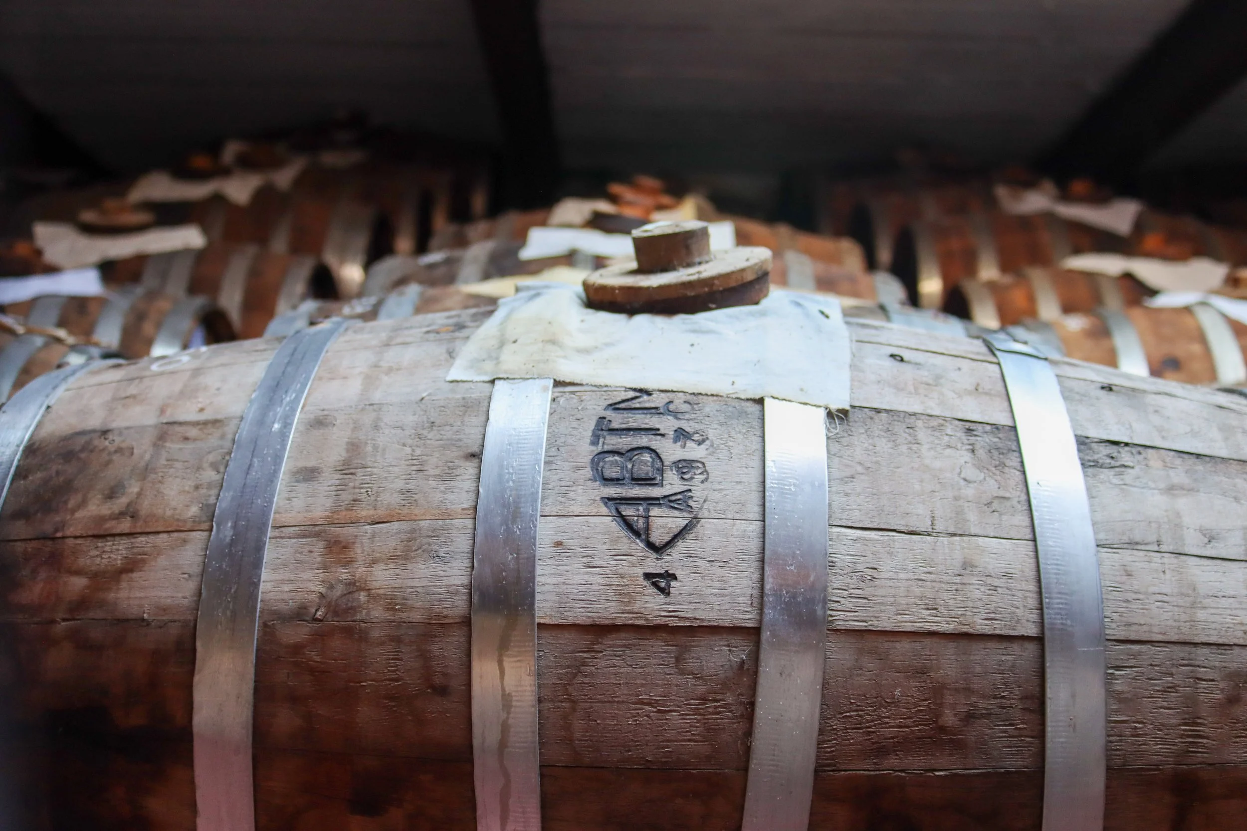 Stacks of wooden barrels stored in a cellar or warehouse, secured with metal hoops.