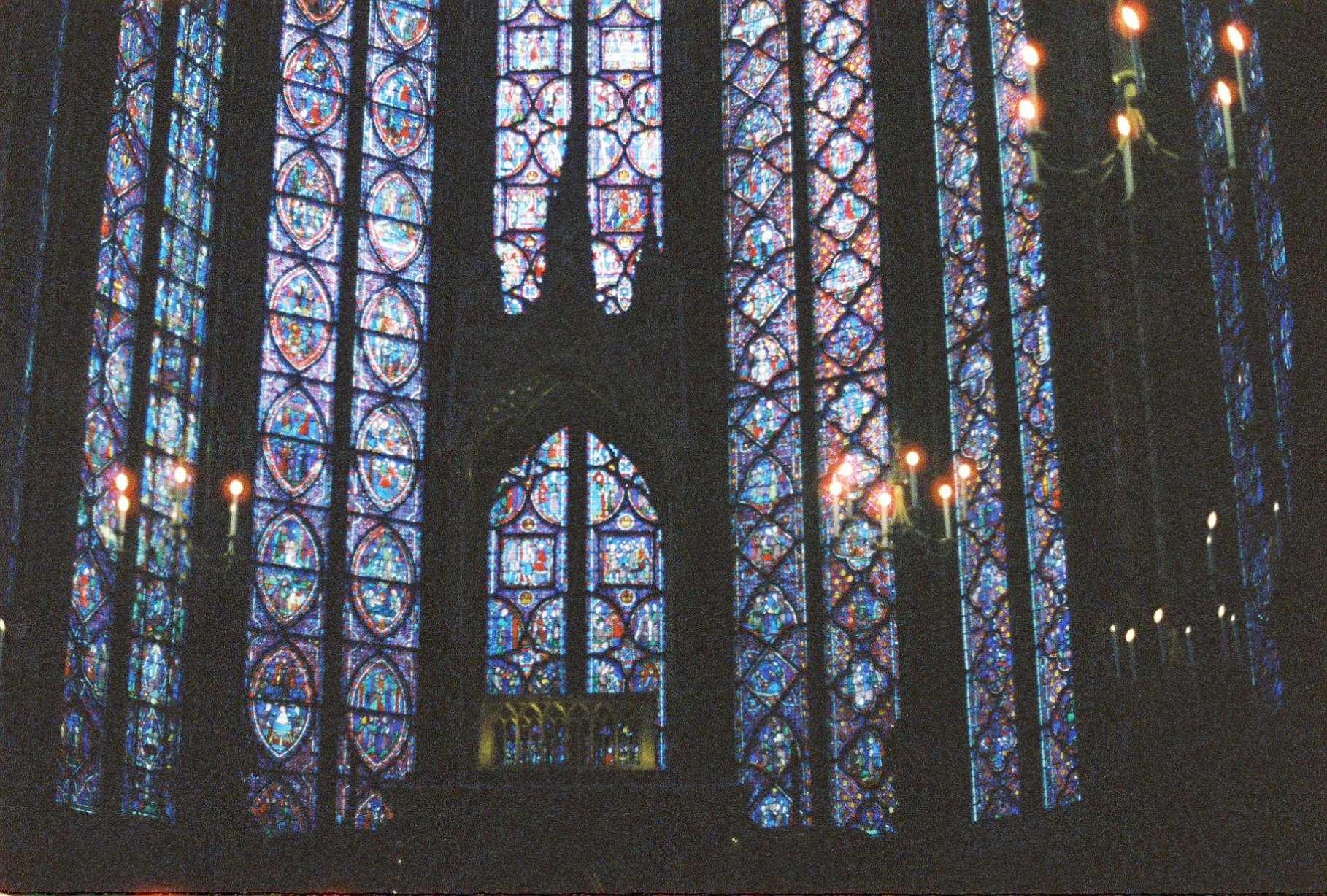 Inside a church with large stained glass windows depicting religious scenes or symbols, illuminated by candlelight.