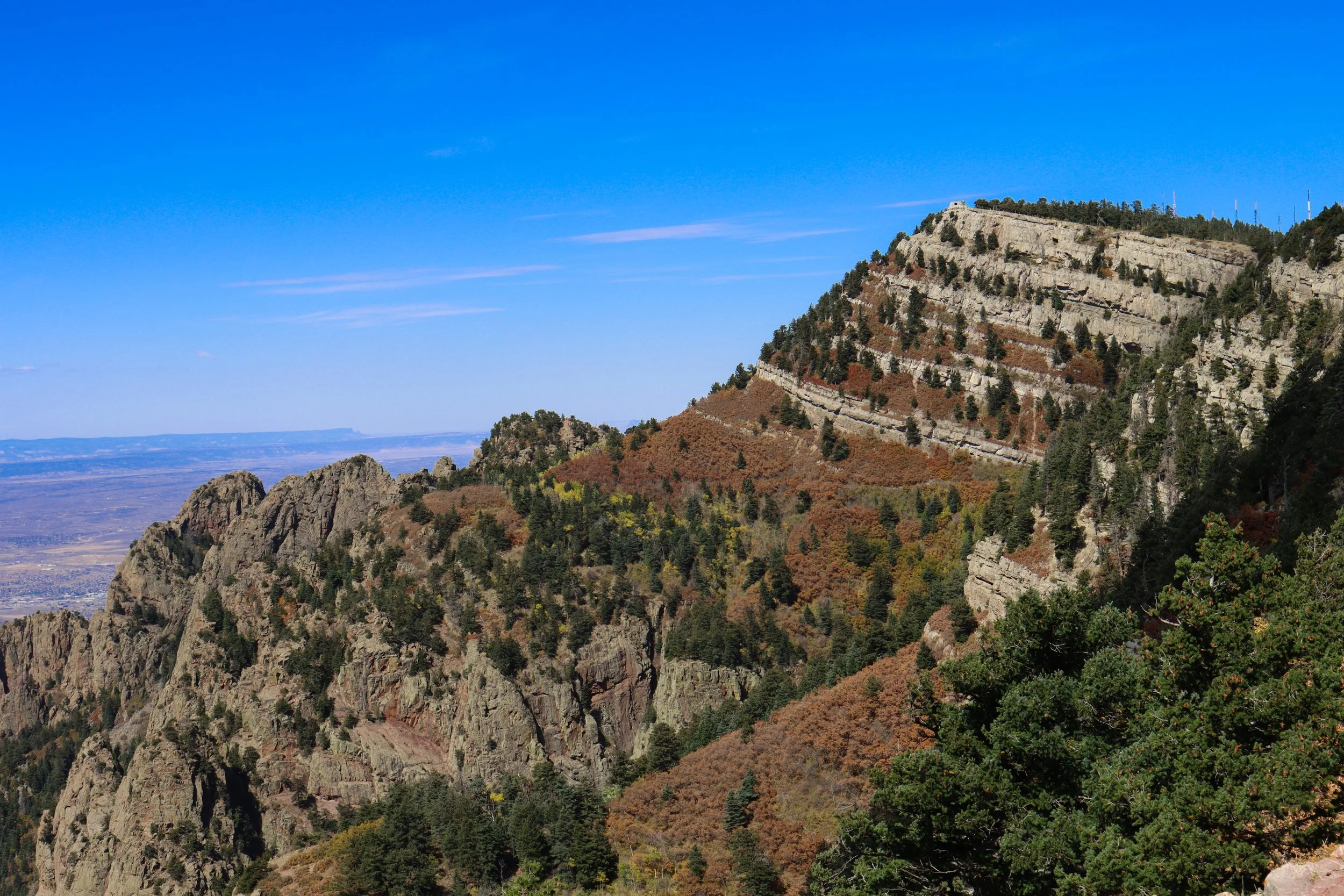 Landscape view of a mountainous area with rocky cliffs and trees, under a clear blue sky.