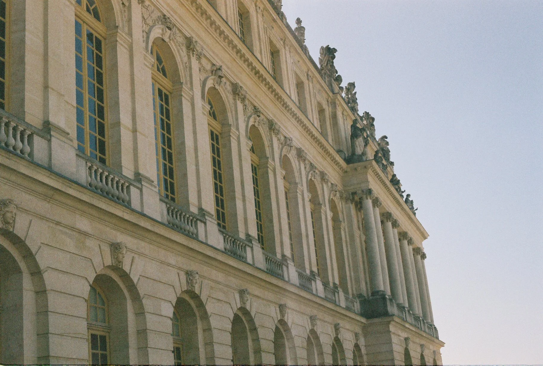 Exterior of a historic building with ornate architectural details, large arched windows, and decorative sculptures on the roofline.