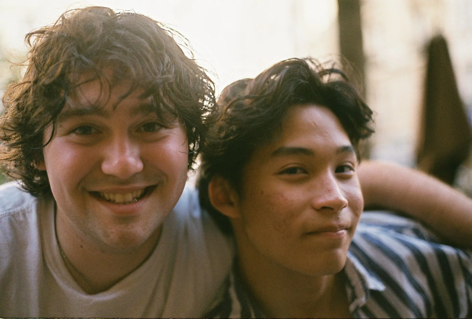 Two young men with curly hair smiling closely together in a casual setting.