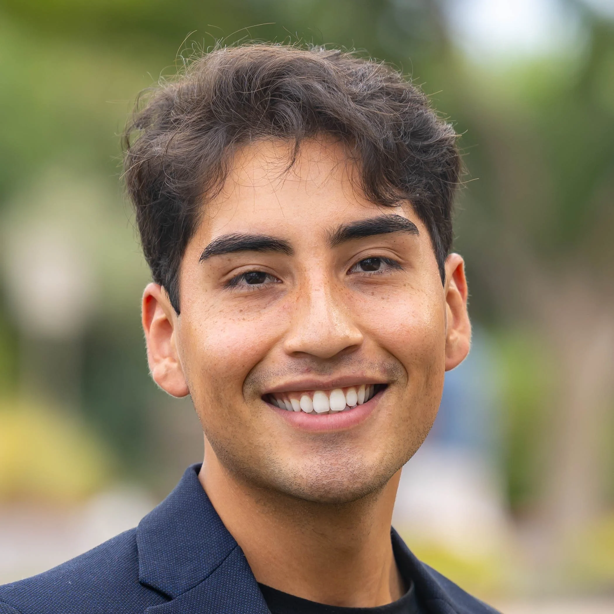 Close-up of a young man smiling outdoors, showing part of his face and tuxedo collar.