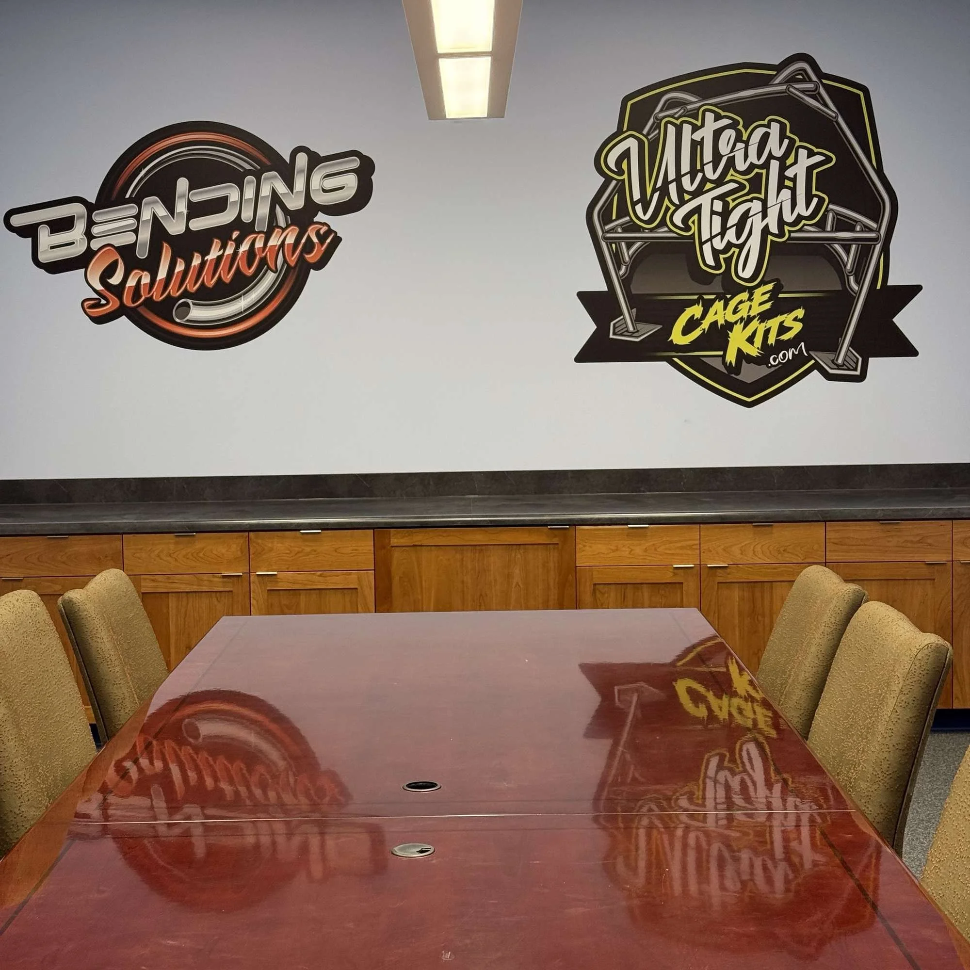 View of a conference room with a reflective wooden table, surrounded by beige chairs, and murals on the wall promoting a company called 'Altria Cigs' or 'Altria Cigarettes.'