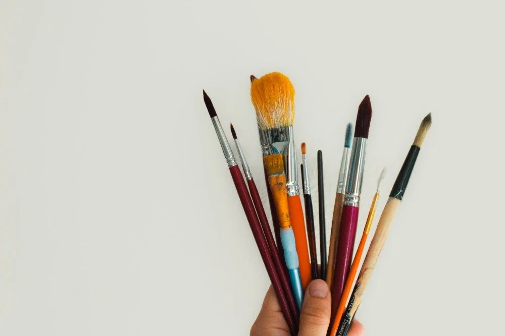 Hand holding a variety of paintbrushes against a plain background.