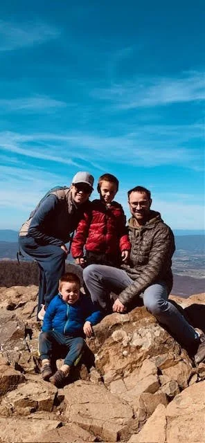 A family of four hiking on rocky terrain with a mountain and blue sky in the background.
