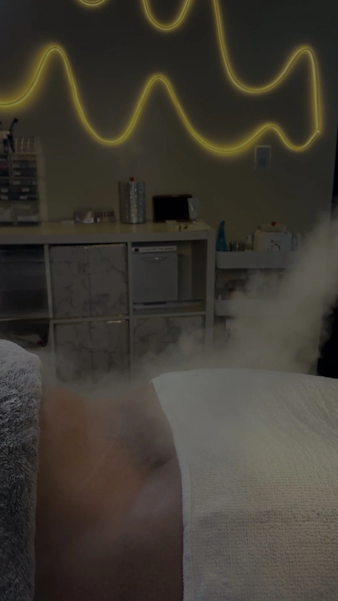Dimly lit room with yellow neon lights on the wall, a counter with various items, and a cloud of steam for a bikini treatment after the best wax in harlem