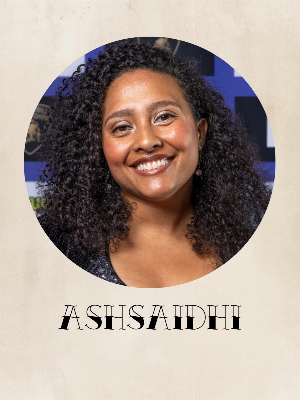 A woman with curly black hair smiling, wearing earrings, and a dark top. The background is blurred with blue and black colors. The text below the image reads "Ashsaidh."