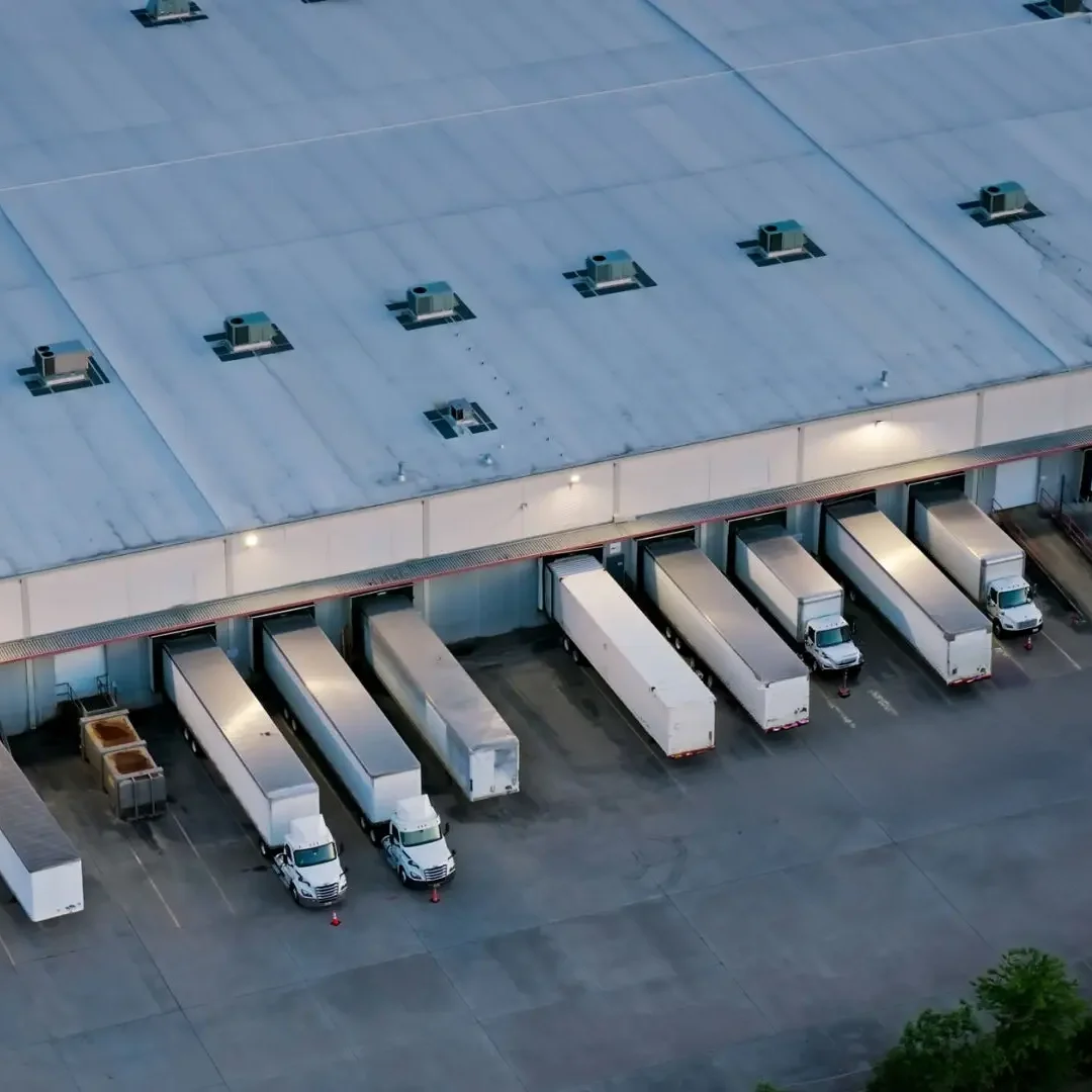 Aerial view of a warehouse loading dock with several trucks parked at the docks, some trucks are white and one is yellow.