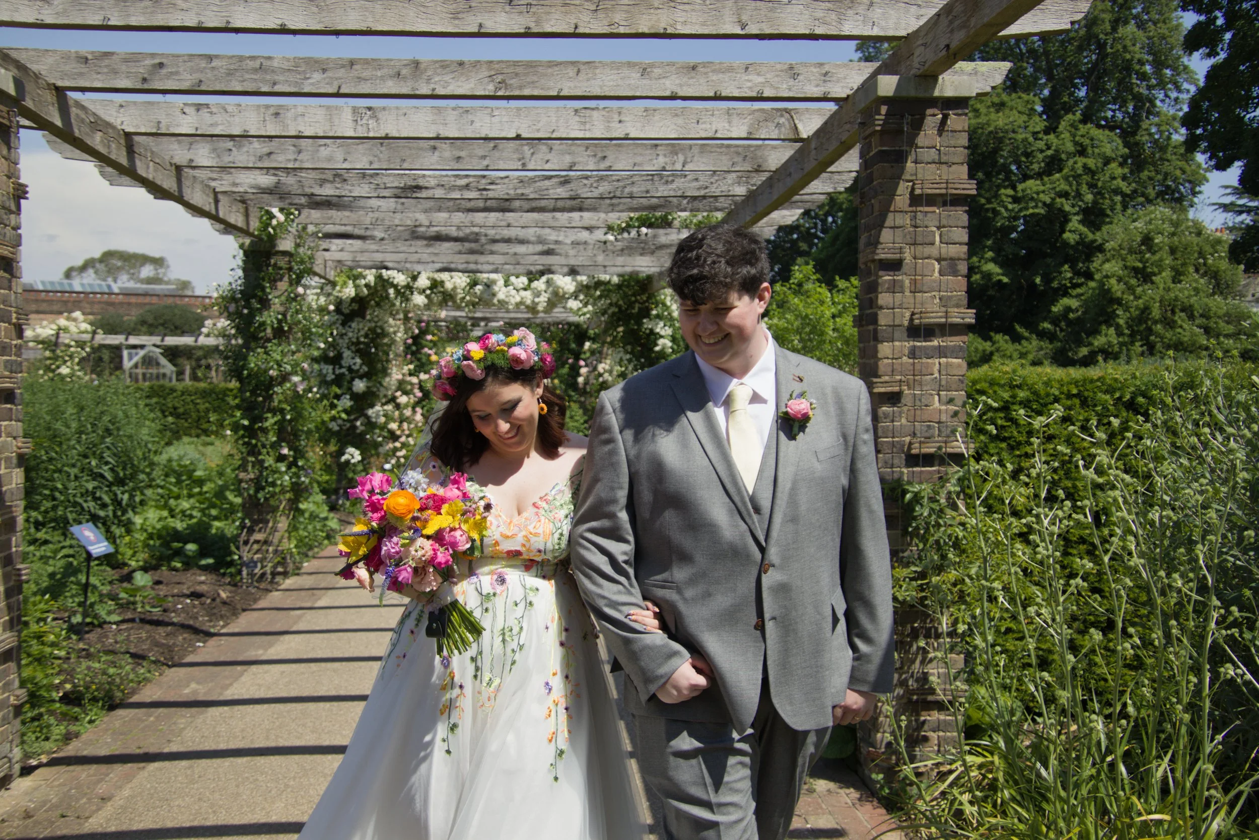A candid photo of a bride and groom looking relaxed and smiling and walking together outdoors in a garden.