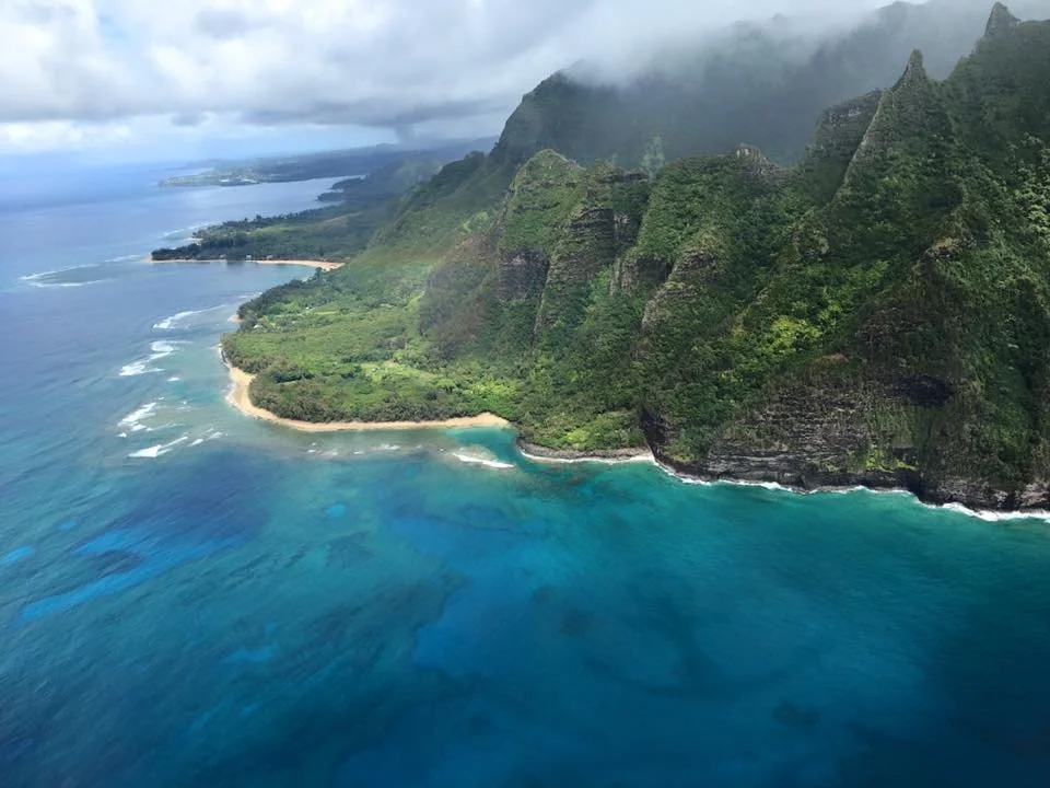 Aerial view of a lush green tropical island with mountains, a sandy beach, and surrounding blue ocean waters.