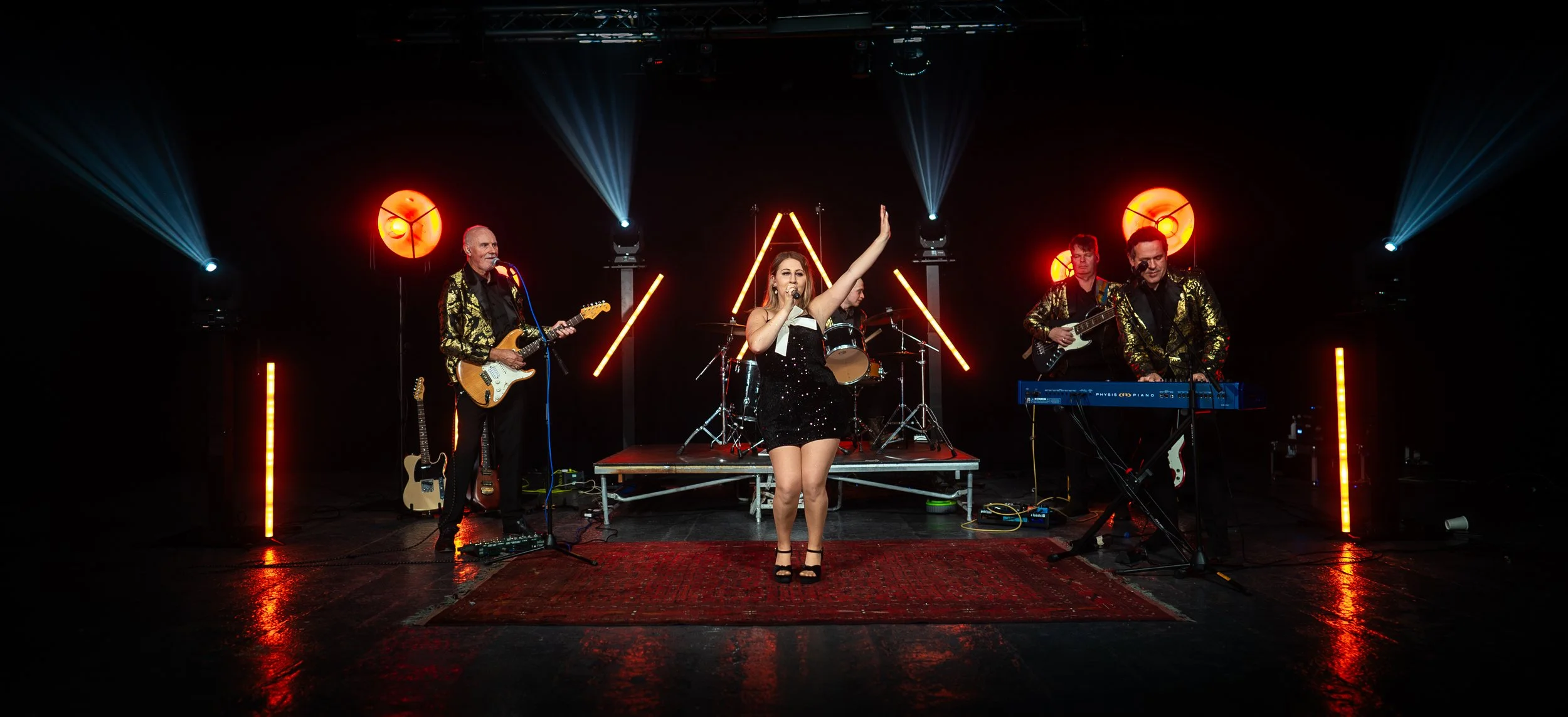 Re-Release wedding band performing on stage with a female lead singer, four male band members, and stage lighting with orange circular lights and neon strip lights in the background.