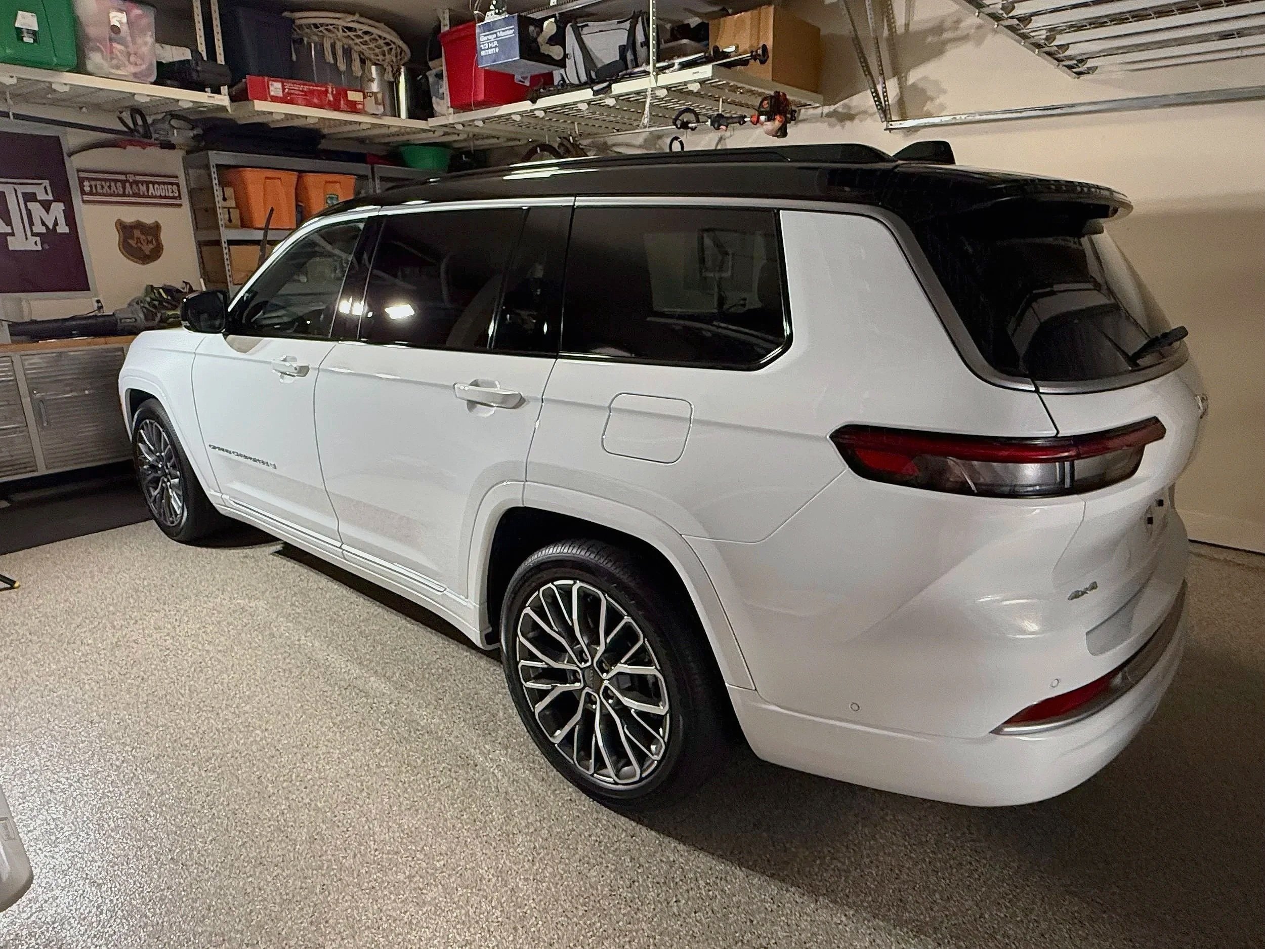 A white SUV with black accents parked inside a garage, with shelves containing various storage boxes and tools in the background.