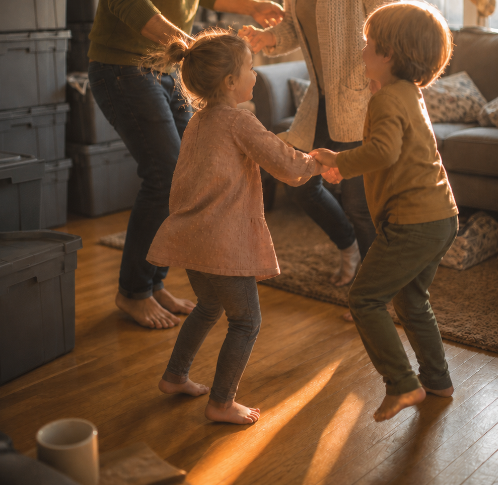 Children dancing and holding hands in a cozy living room with sunlight streaming in.
