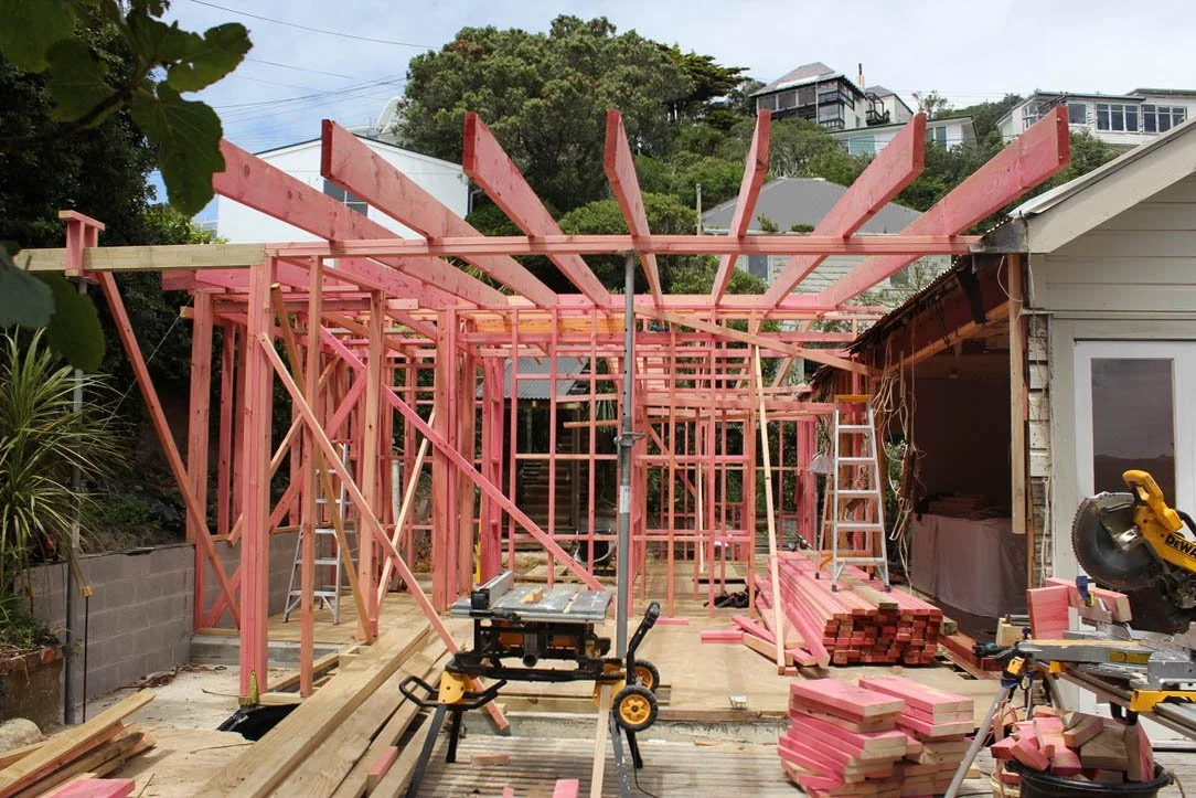 Wood framing construction of a house extension or addition, with pink insulation material on site, in progress, with tools and building materials around.