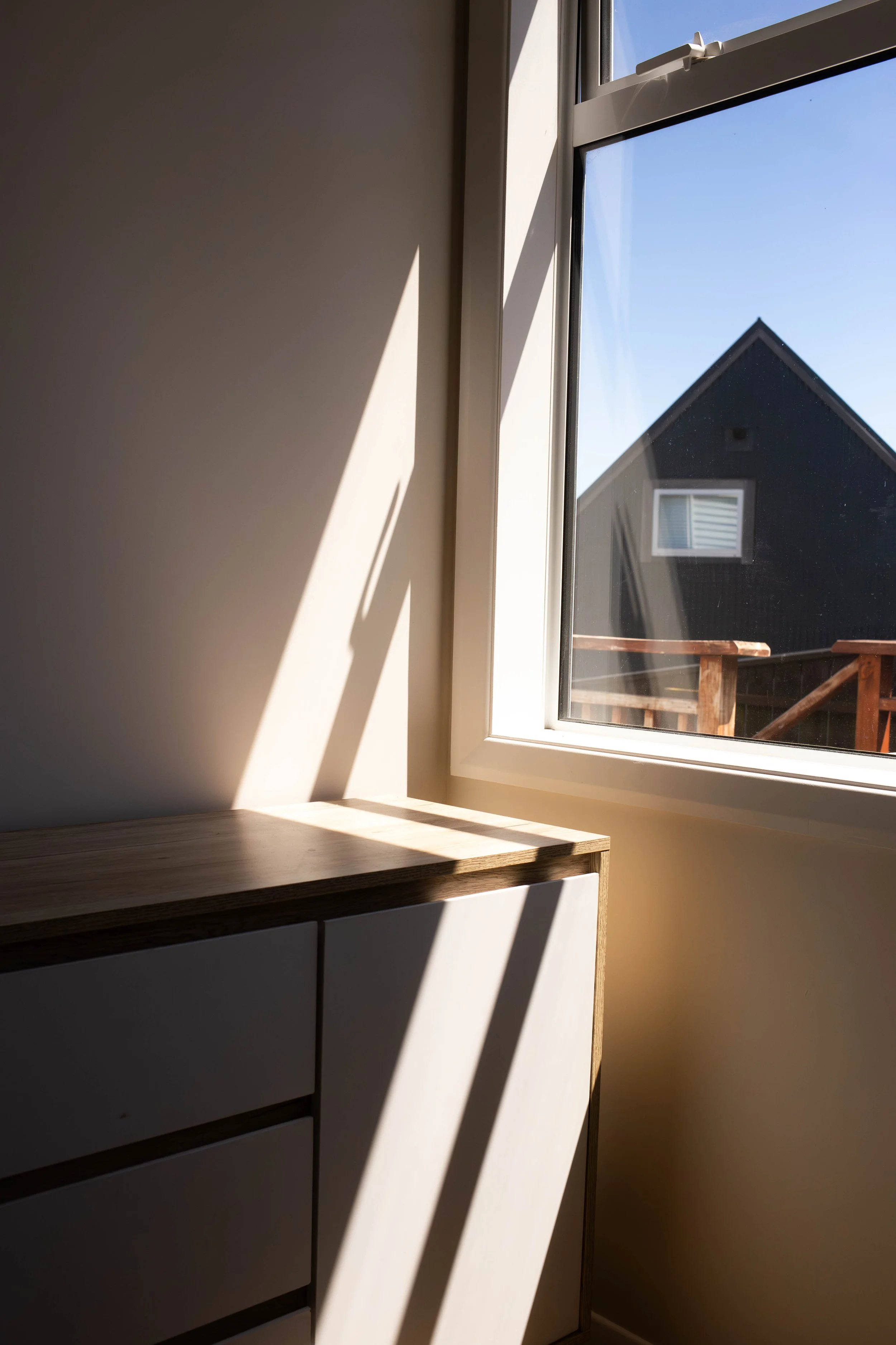 Sunlight casting shadows on the wall and cabinet beside a window in a room.