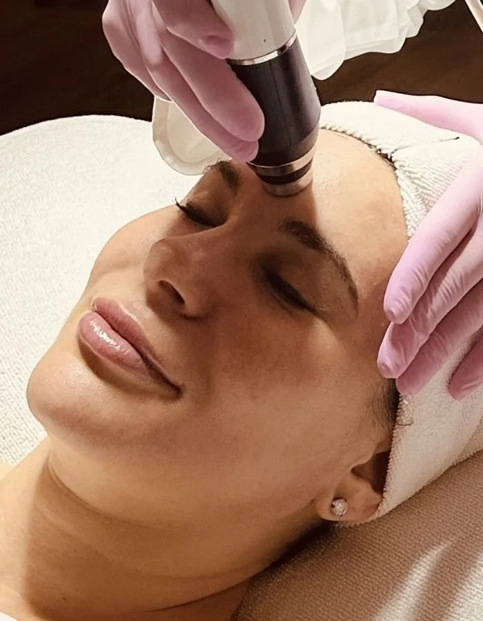 A woman receives a Glo2 facial at Avila Skin Studio in McKinney, lying on a treatment bed with her eyes closed.