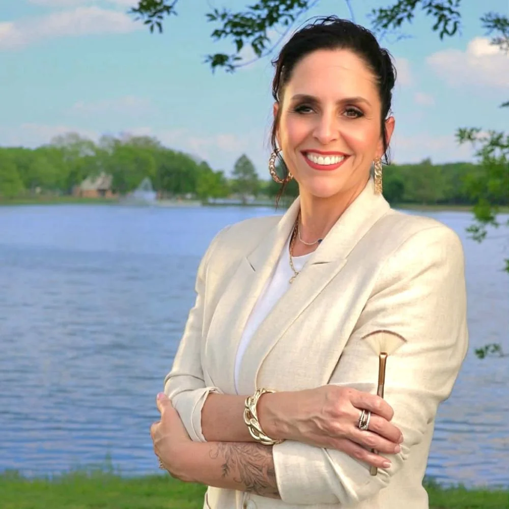 Amy Avila owner of Avila Skin Studio poses in front of a lake holding a facial brush