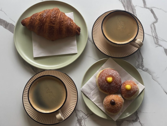 A croissant on a green plate, two cups of coffee, and four donuts on a napkin.