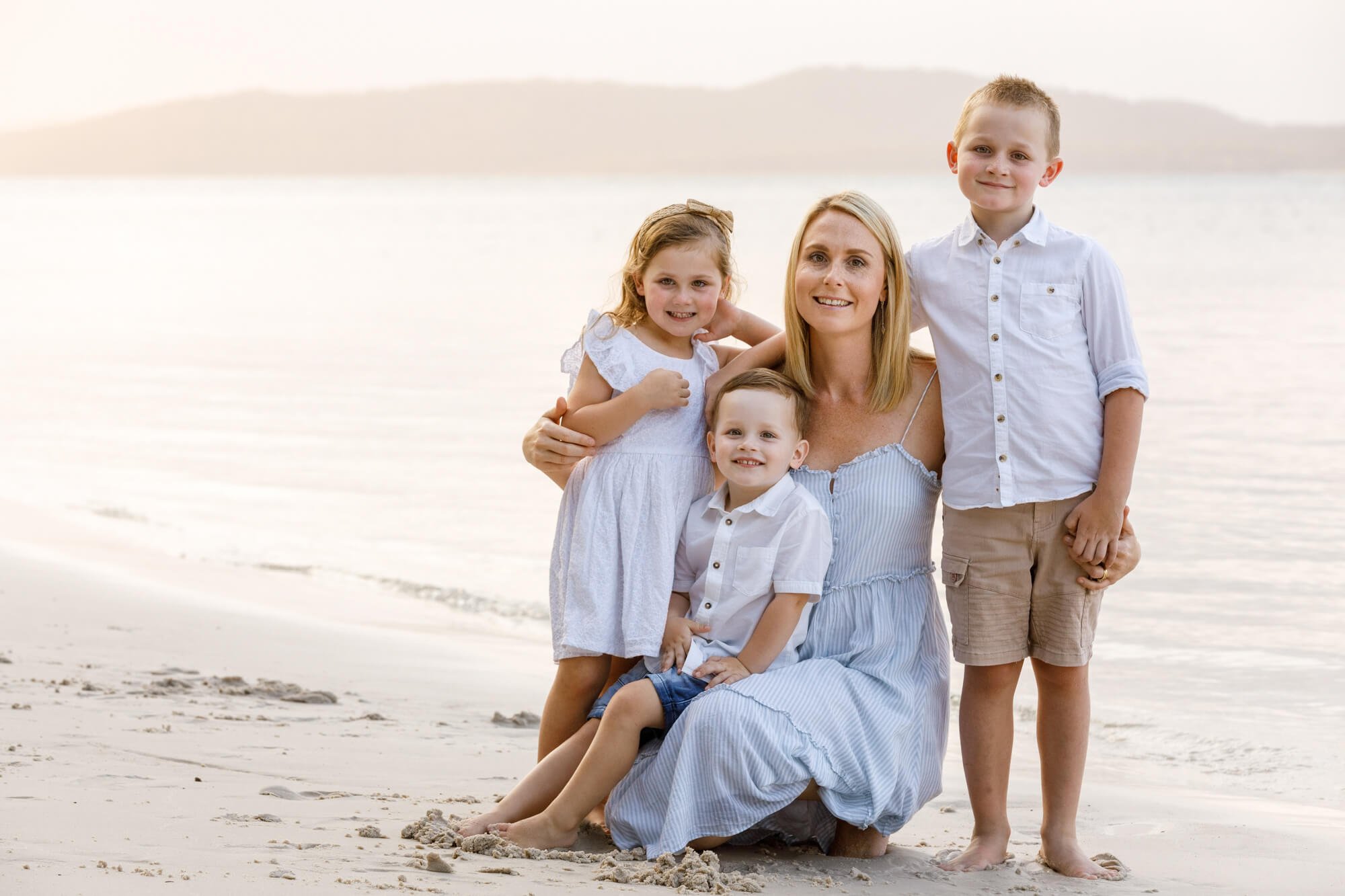 Mother with her three young children posing together on the beach in soft golden light, Bagnalls Beach, Corlette, Port Stephens.