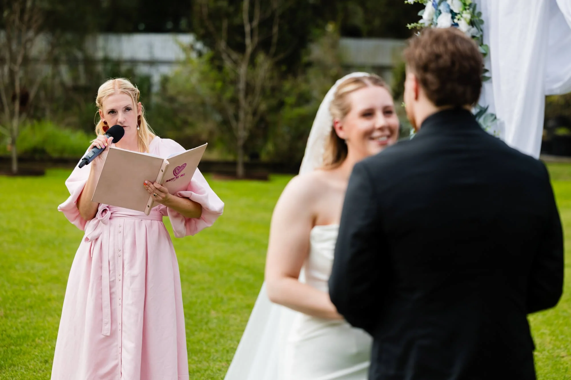 Celebrant Mel, in a pink dress, reading vows to the couple on the lawn during their elopement ceremony.