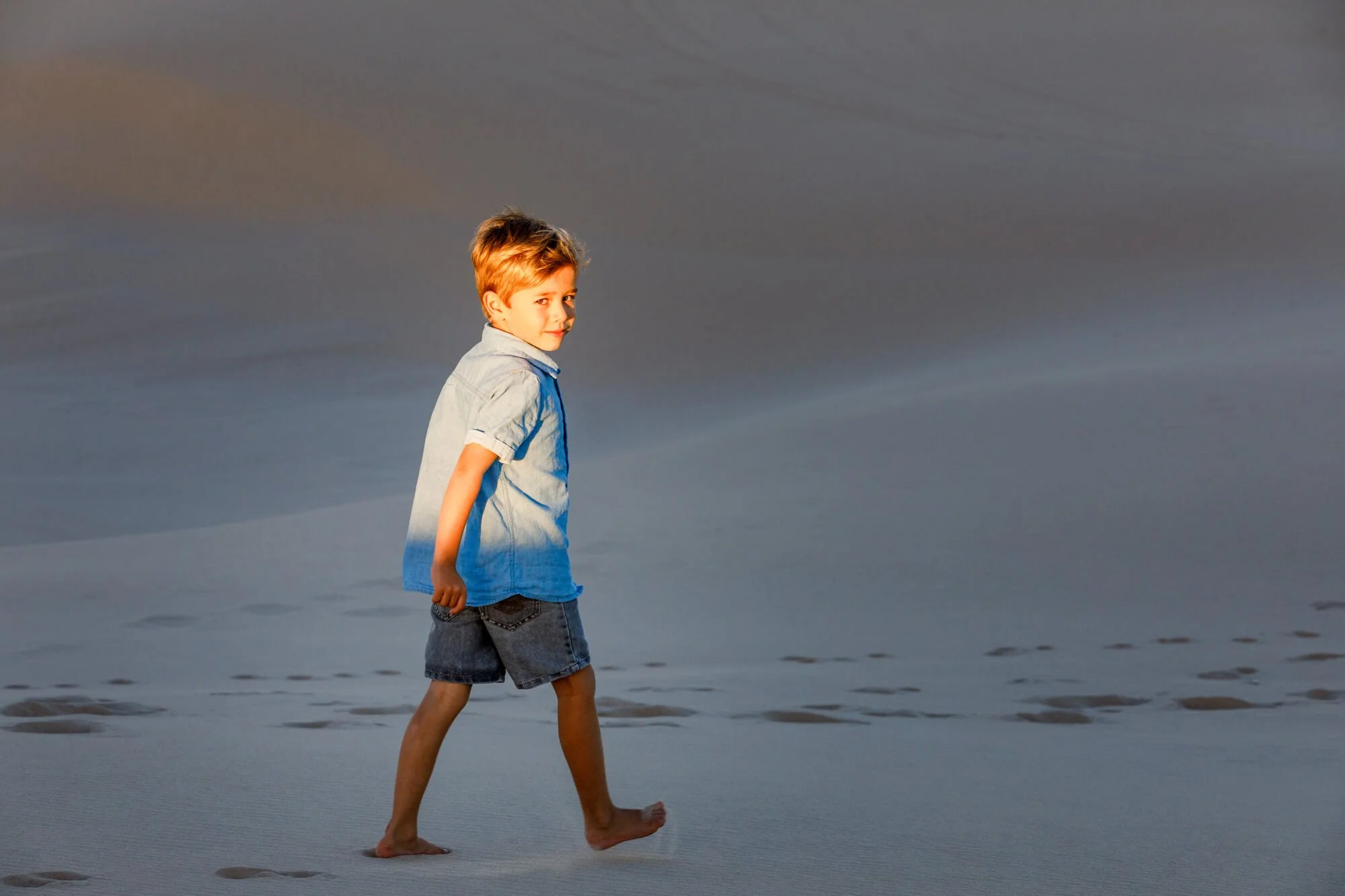 Young boy walking along the beach at dusk in soft blue and orange light, caught mid-stride, Anaa Bay sand dunes, Port Stephens.